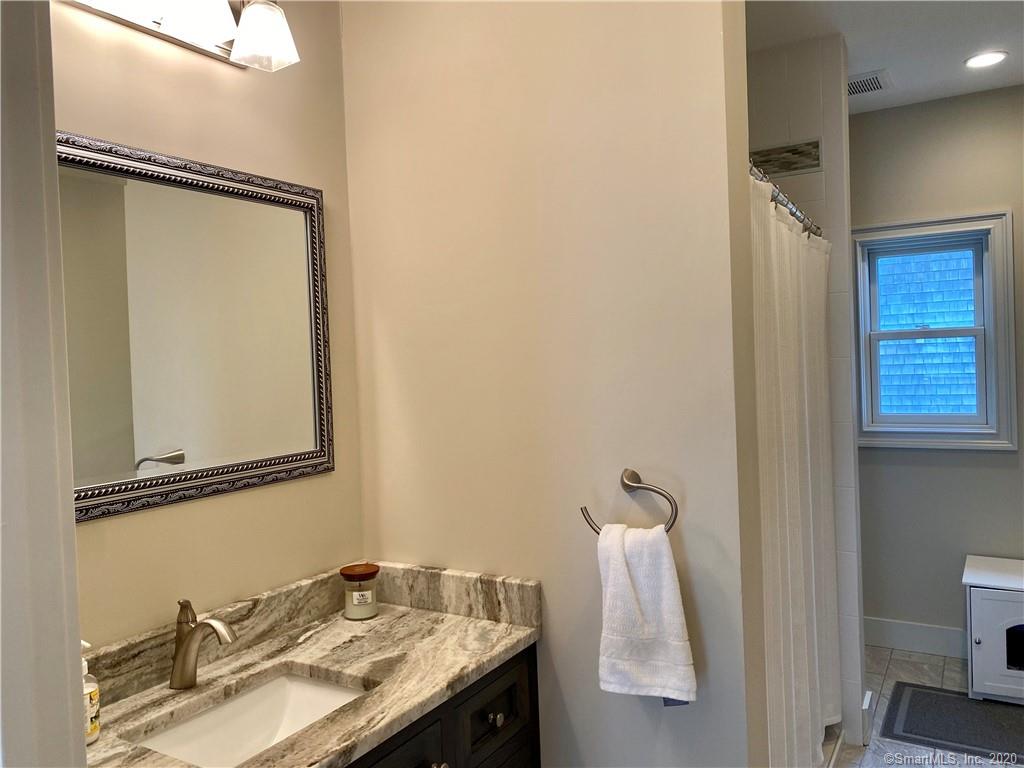 Bathroom with granite countertop, mirror, shower, window, and towel rack.