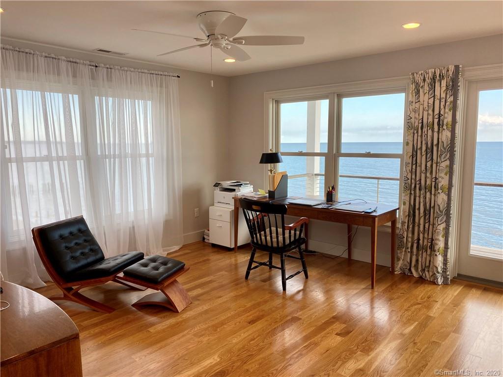 Bright room with hardwood floors, a desk facing a water view, and a modern lounge chair.