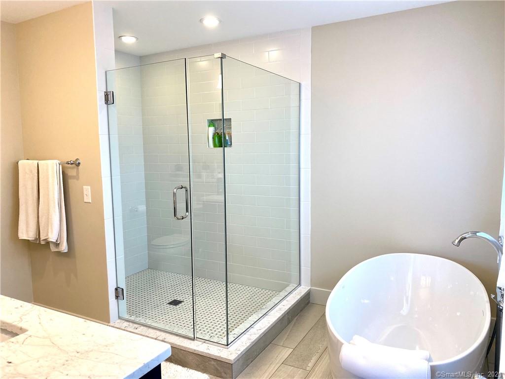 Modern bathroom with glass shower, white tub, and neutral walls.