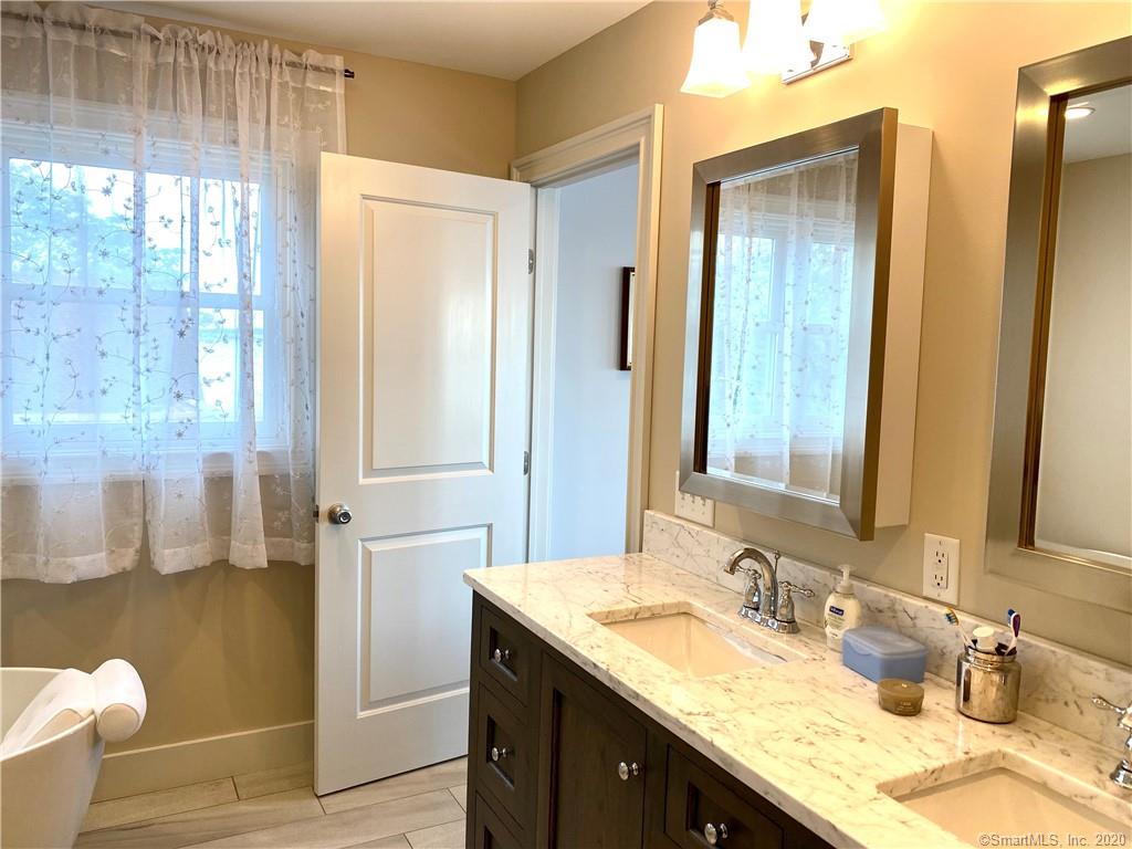 Bathroom with double vanity, white countertops, and window with sheer curtains.