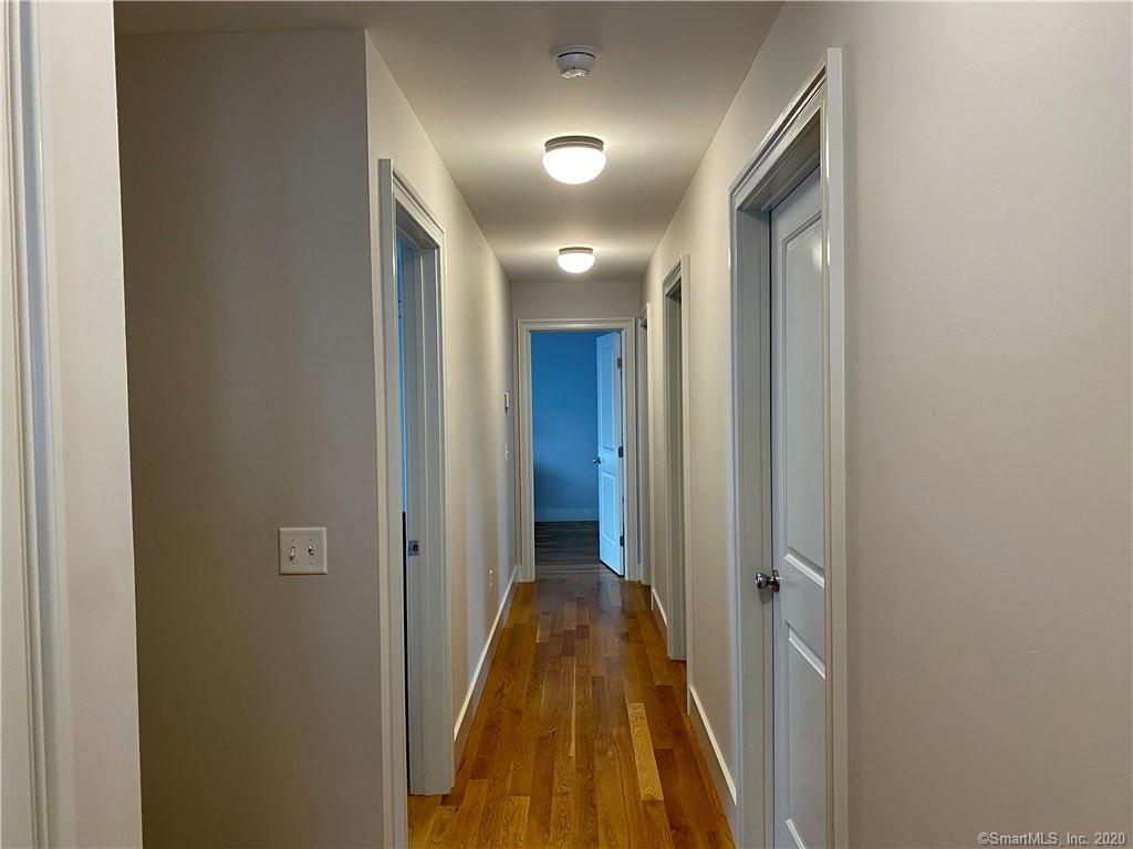 Narrow hallway with wood floors, doors on both sides, and ceiling lights.