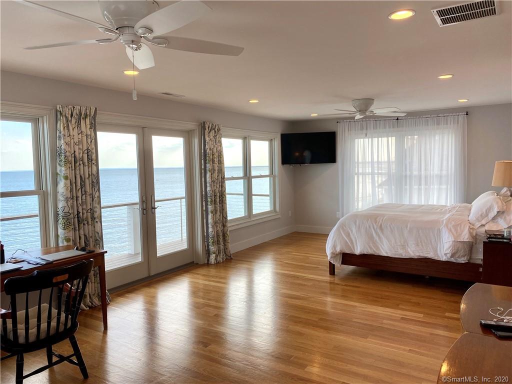 Spacious bedroom with water view, wood floors, bed, desk, and French doors.