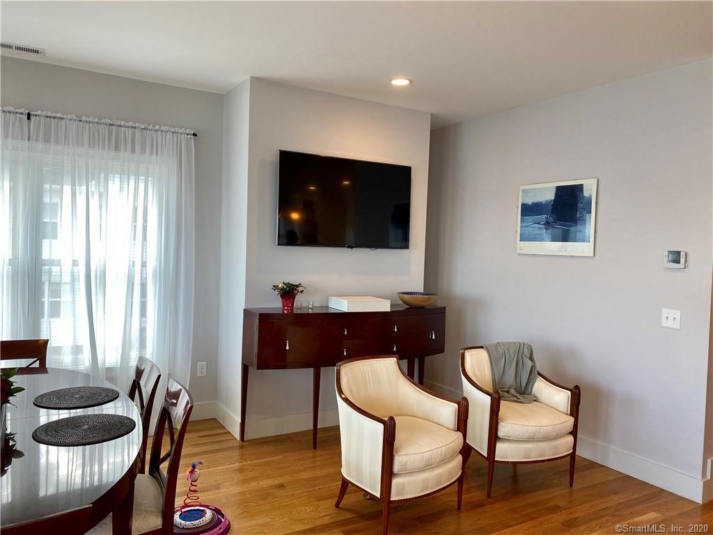 Living room with TV above a dark wood cabinet, two cream chairs, and a window with white curtains.