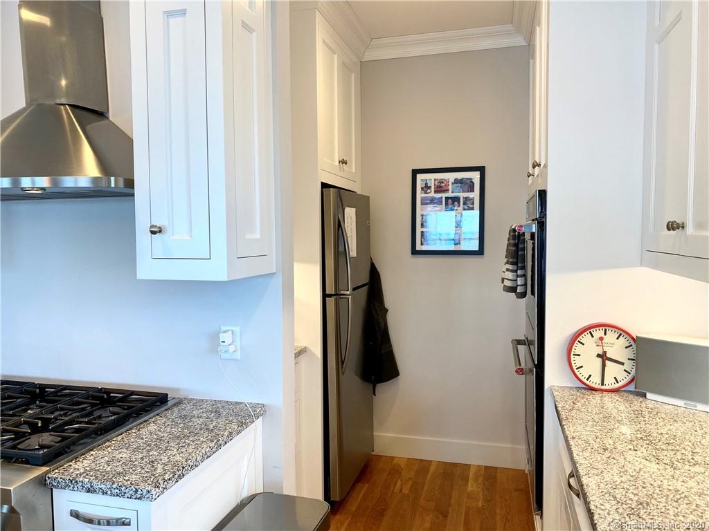 Narrow kitchen with white cabinets, stainless steel appliances, and a red clock.