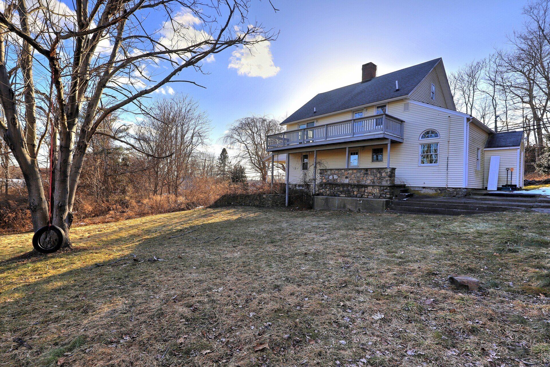 Yellow house with a balcony and a tire swing in a yard on a sunny day.