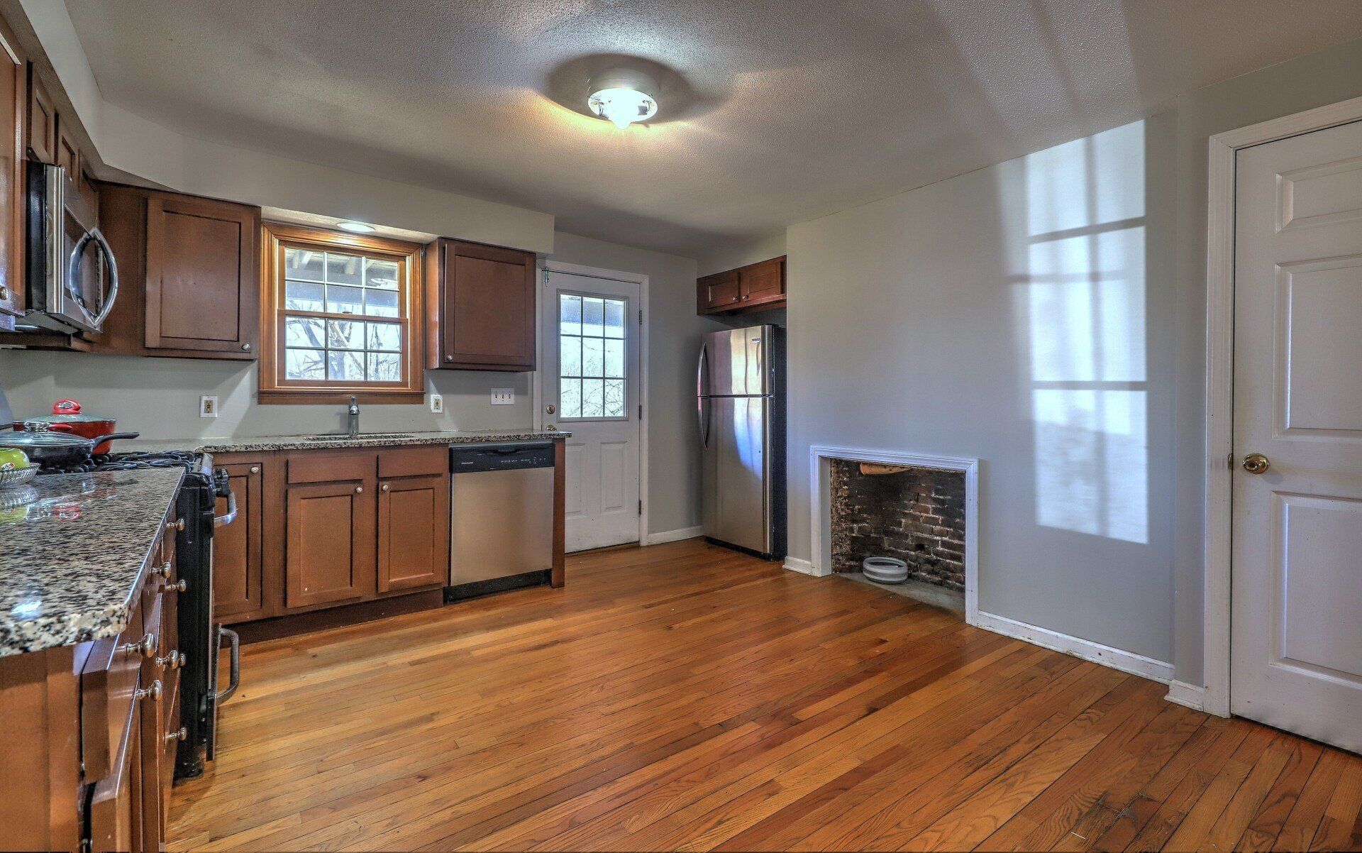 Kitchen with hardwood floors, wooden cabinets, stainless steel appliances, and a small fireplace.