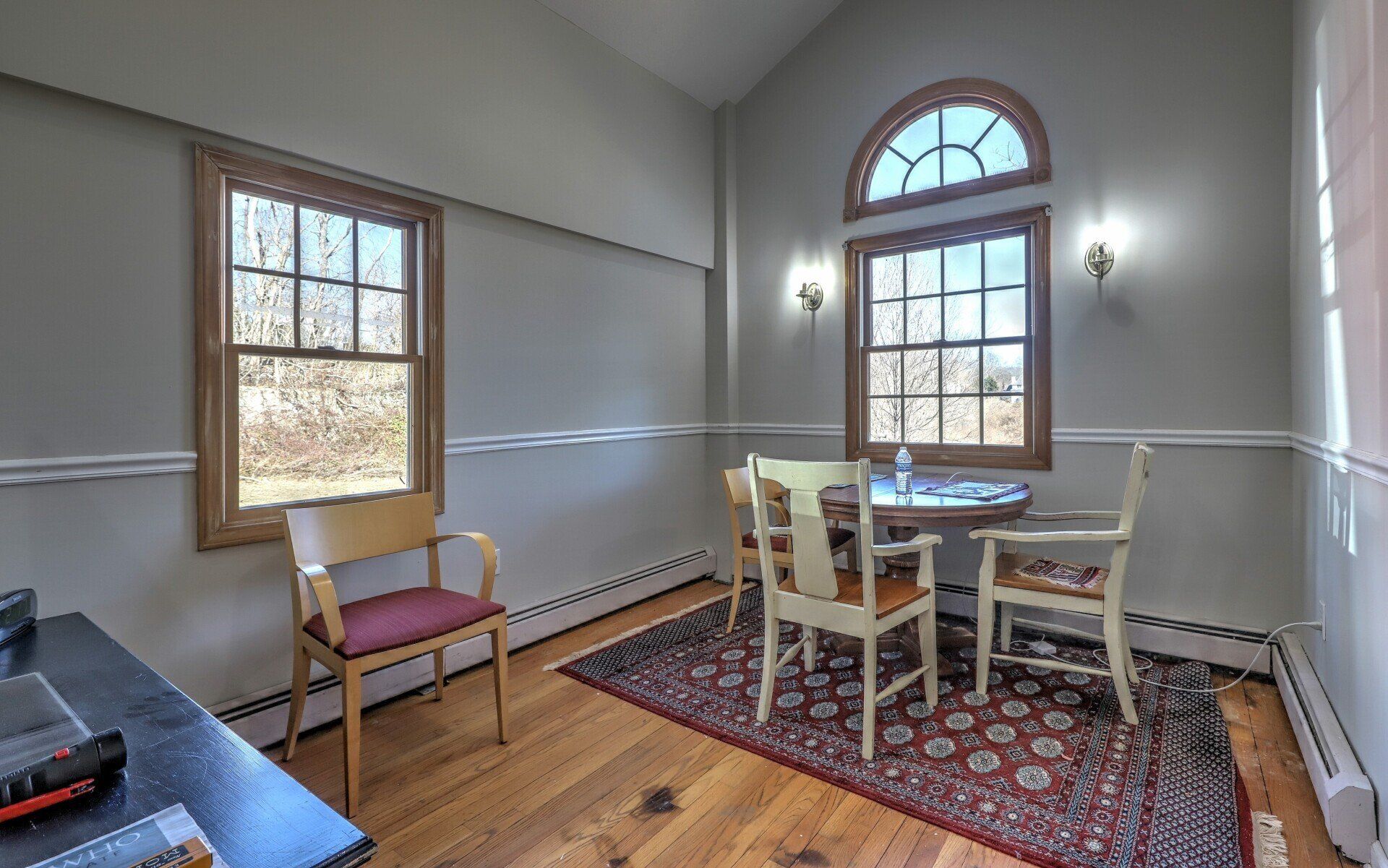 Dining room: table with chairs, two windows, rug, light walls, and wooden floors.