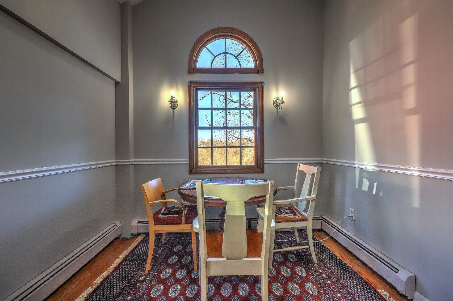 A small dining room with a table, chairs, and a window with sunlight streaming through.