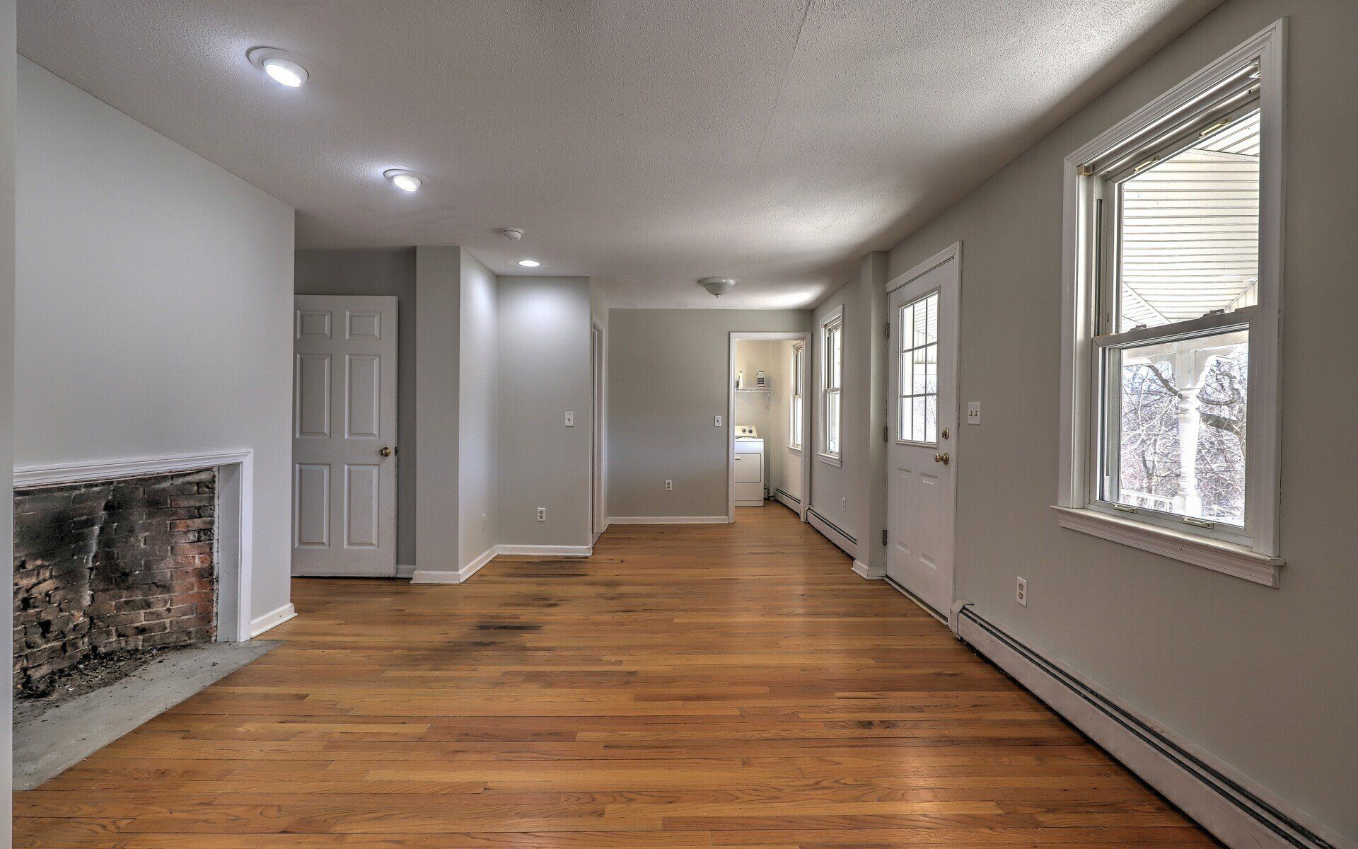 Empty living room with wood floors, fireplace, and two doorways.