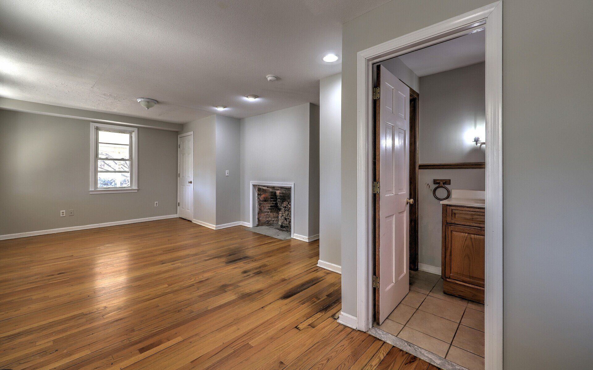 Empty room with hardwood floors, fireplace, and bathroom doorway.