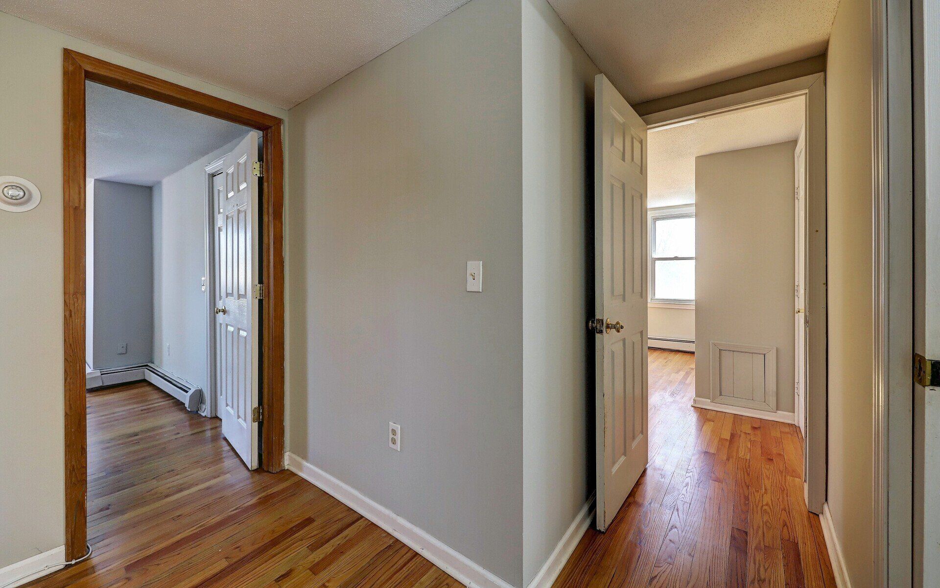 Hallway with open doors leading to rooms with hardwood floors.