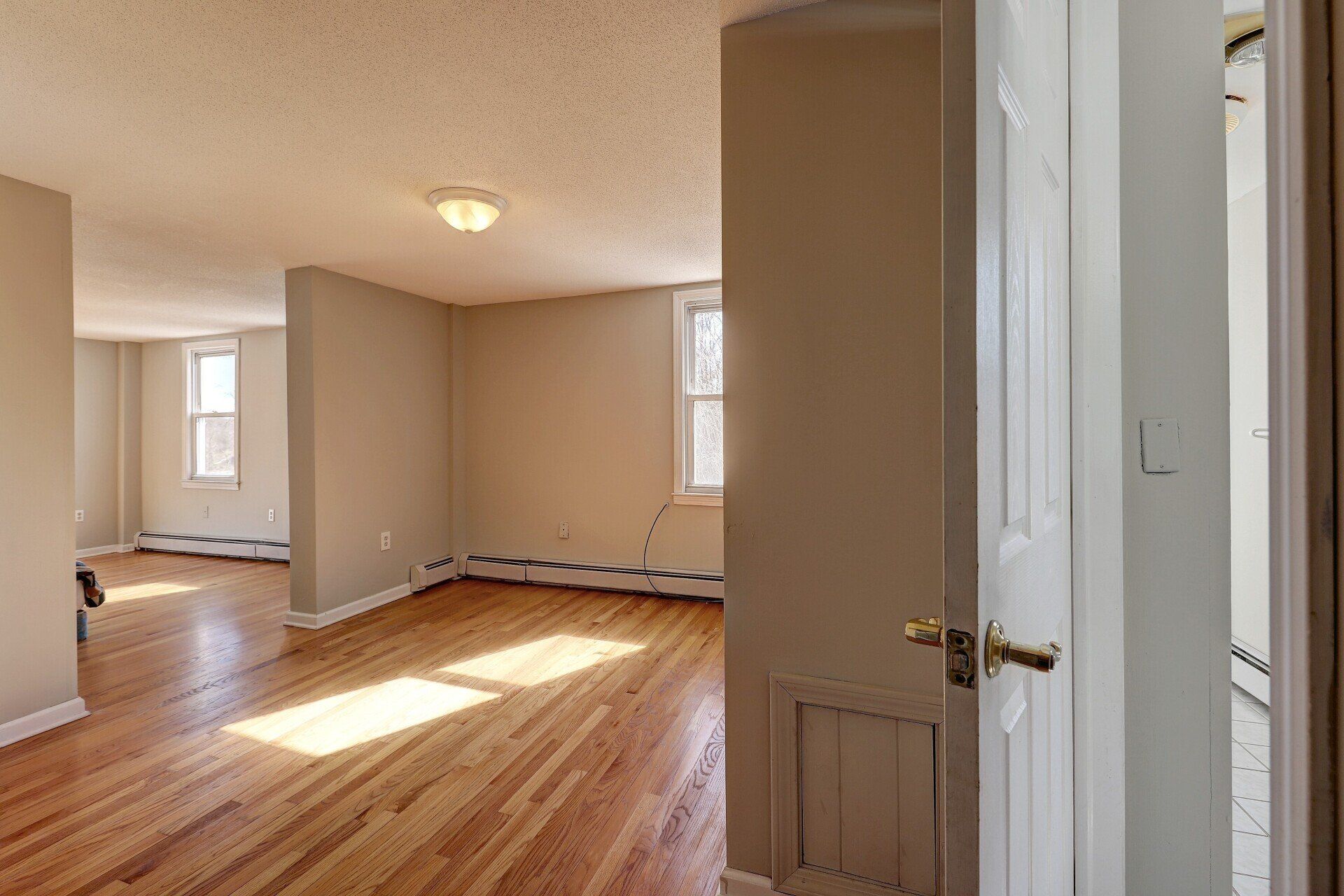 Interior view of a light-filled apartment with wood floors, neutral walls, and open doorways.