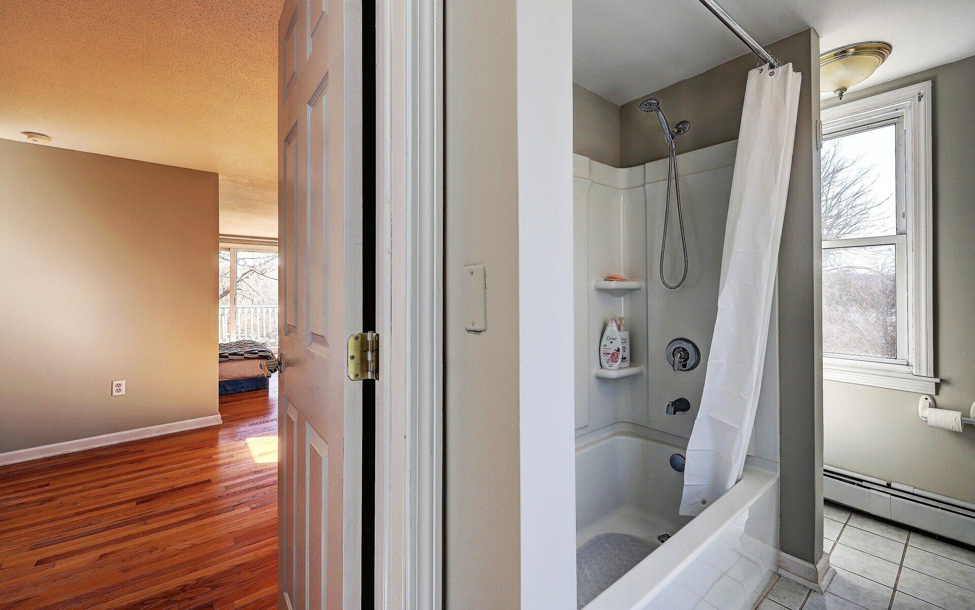 Doorway into bedroom with hardwood floors, bathroom with tub and window.