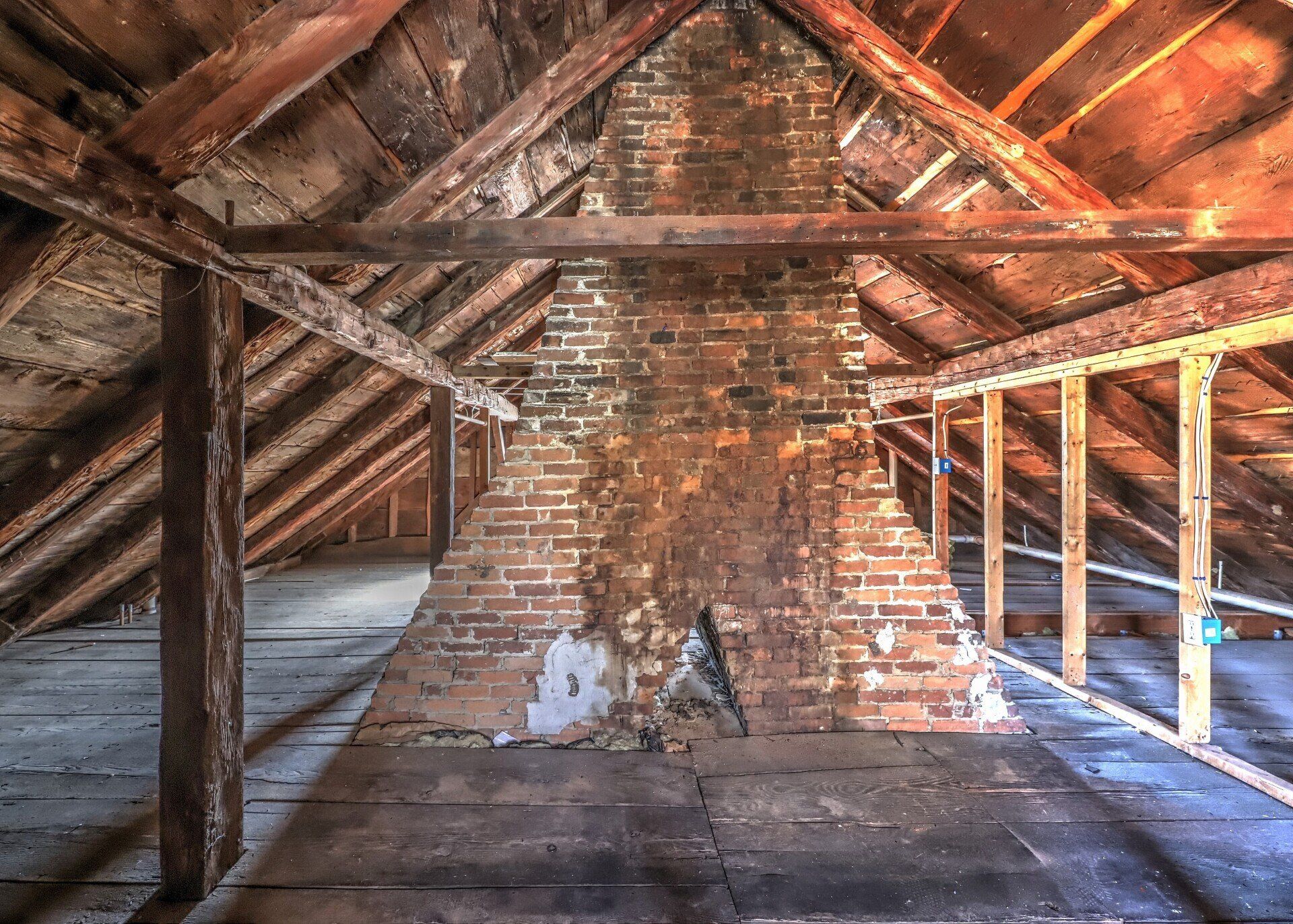 Attic interior with exposed wood framing, a brick chimney, and dark shadows.