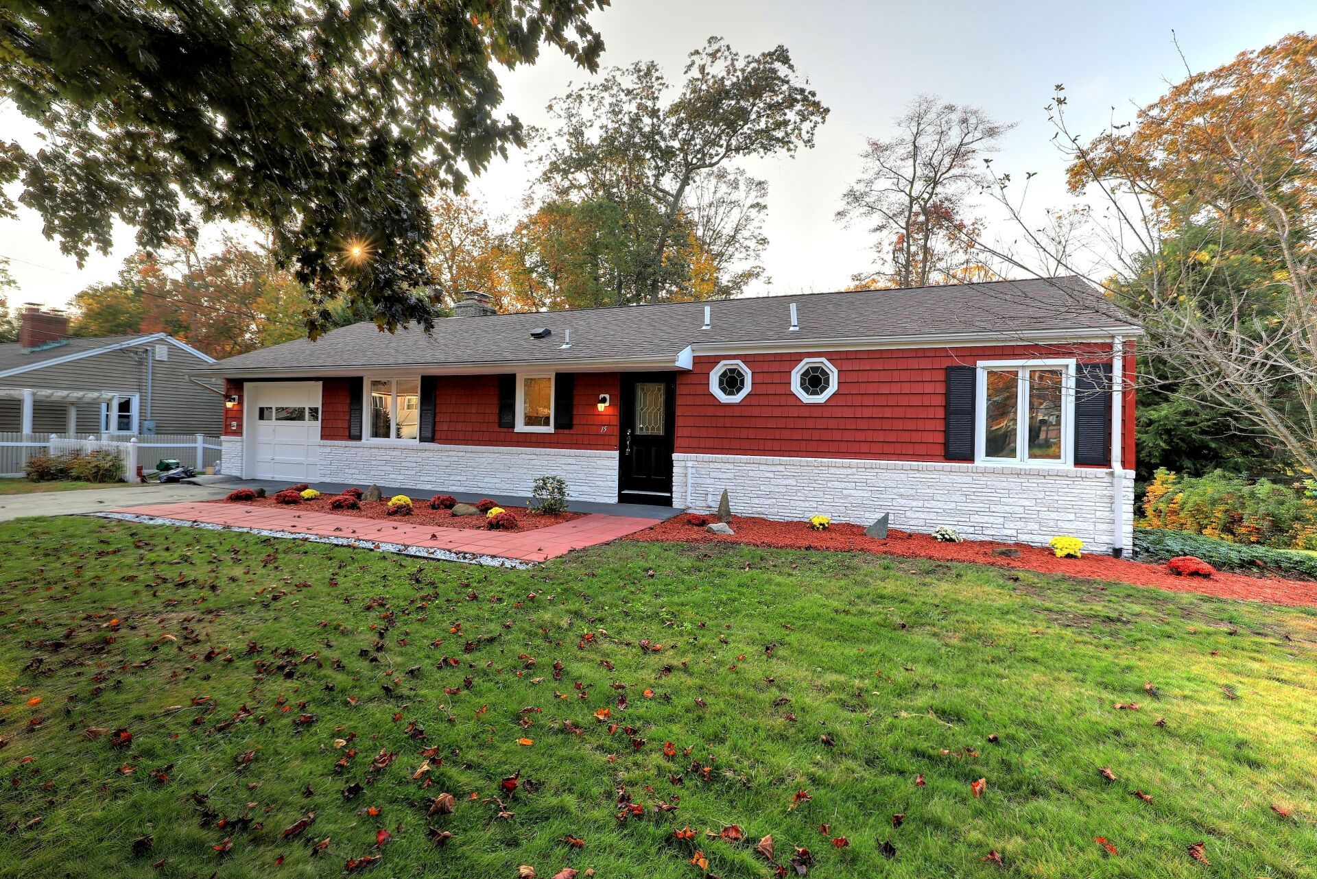 Red and white ranch house with black shutters, circular windows, and a green lawn.