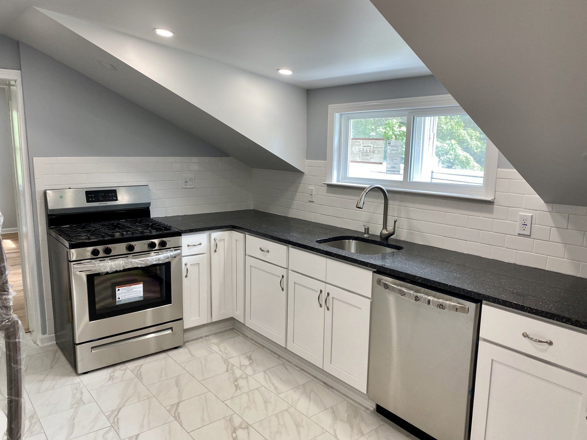 A modern kitchen with stainless steel appliances, white cabinets, black countertop, and a window.