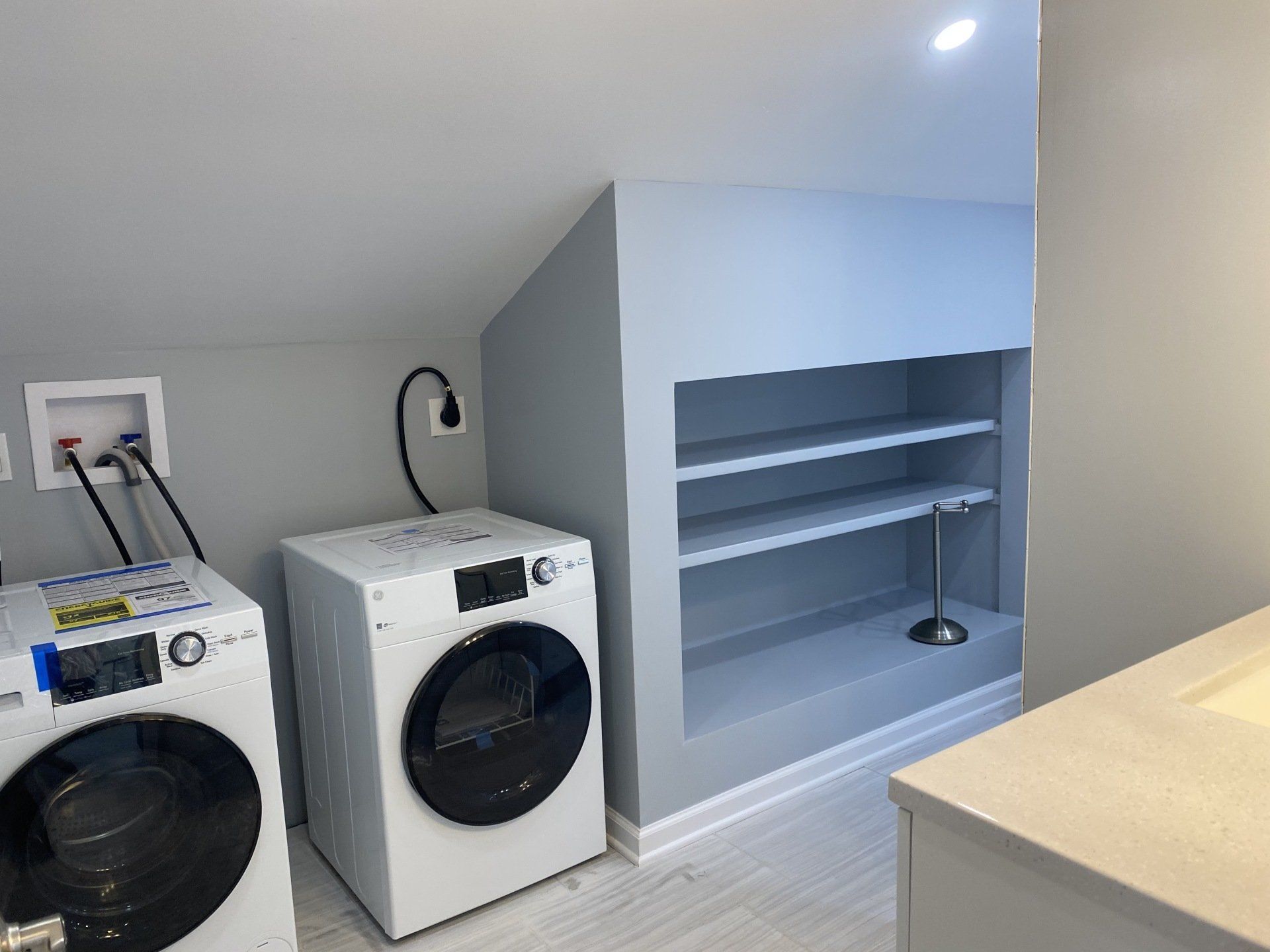 Laundry room with gray walls, white washer/dryer, and built-in shelving.