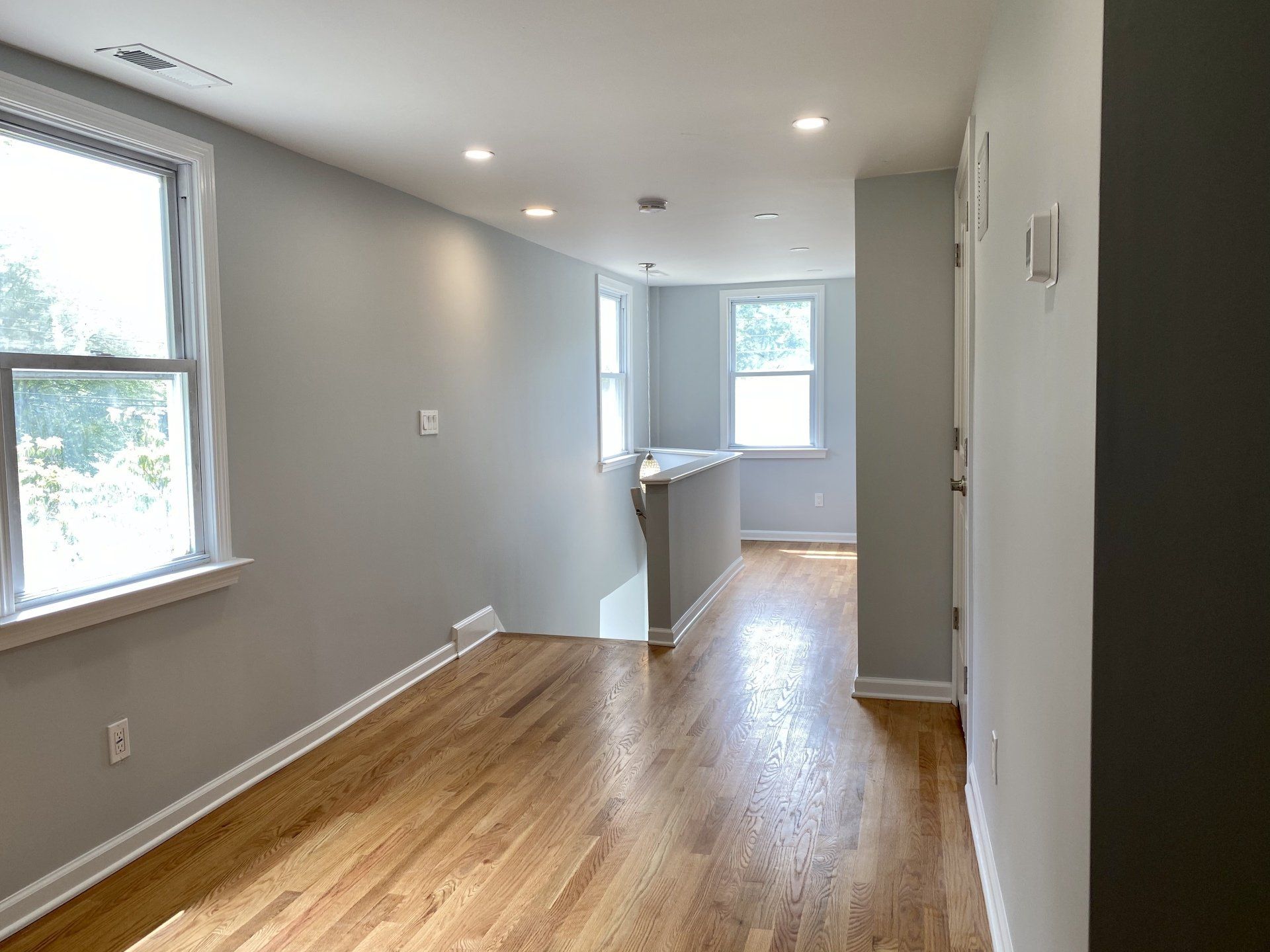 Interior view of a house with hardwood floors, gray walls, and bright windows.