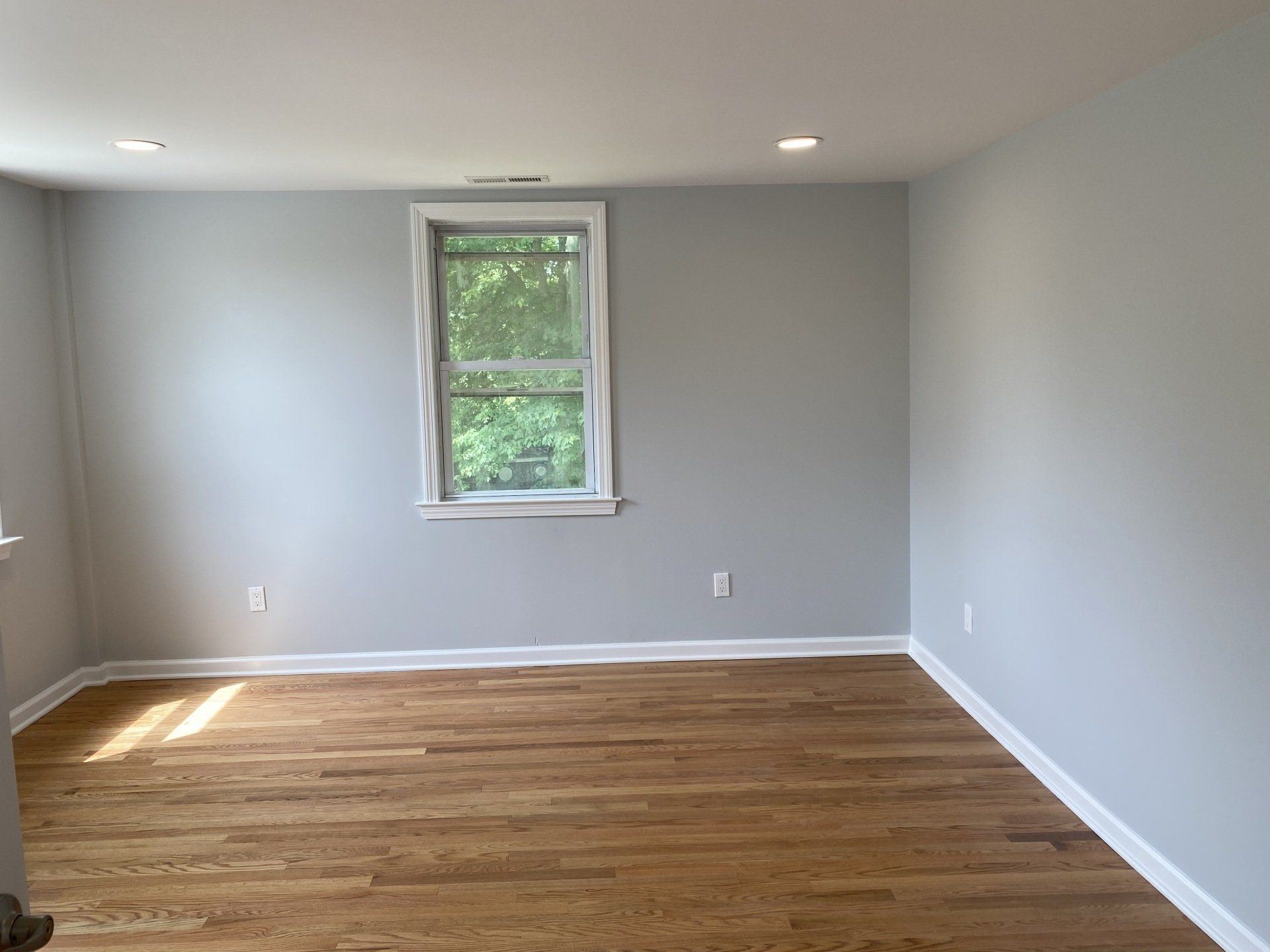 Empty room with gray walls, hardwood floor, window, and recessed lighting.