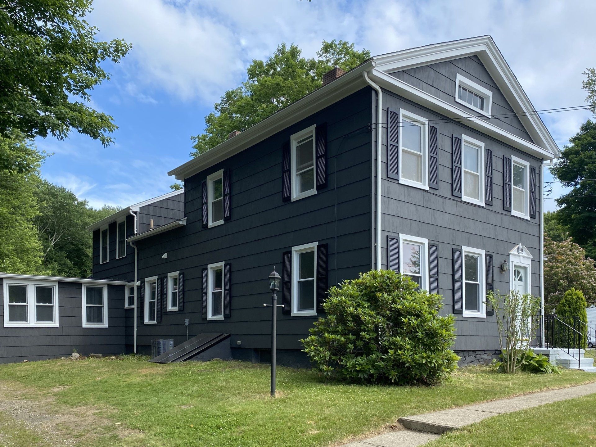 Gray two-story house with black shutters, white trim, and a small front yard on a sunny day.