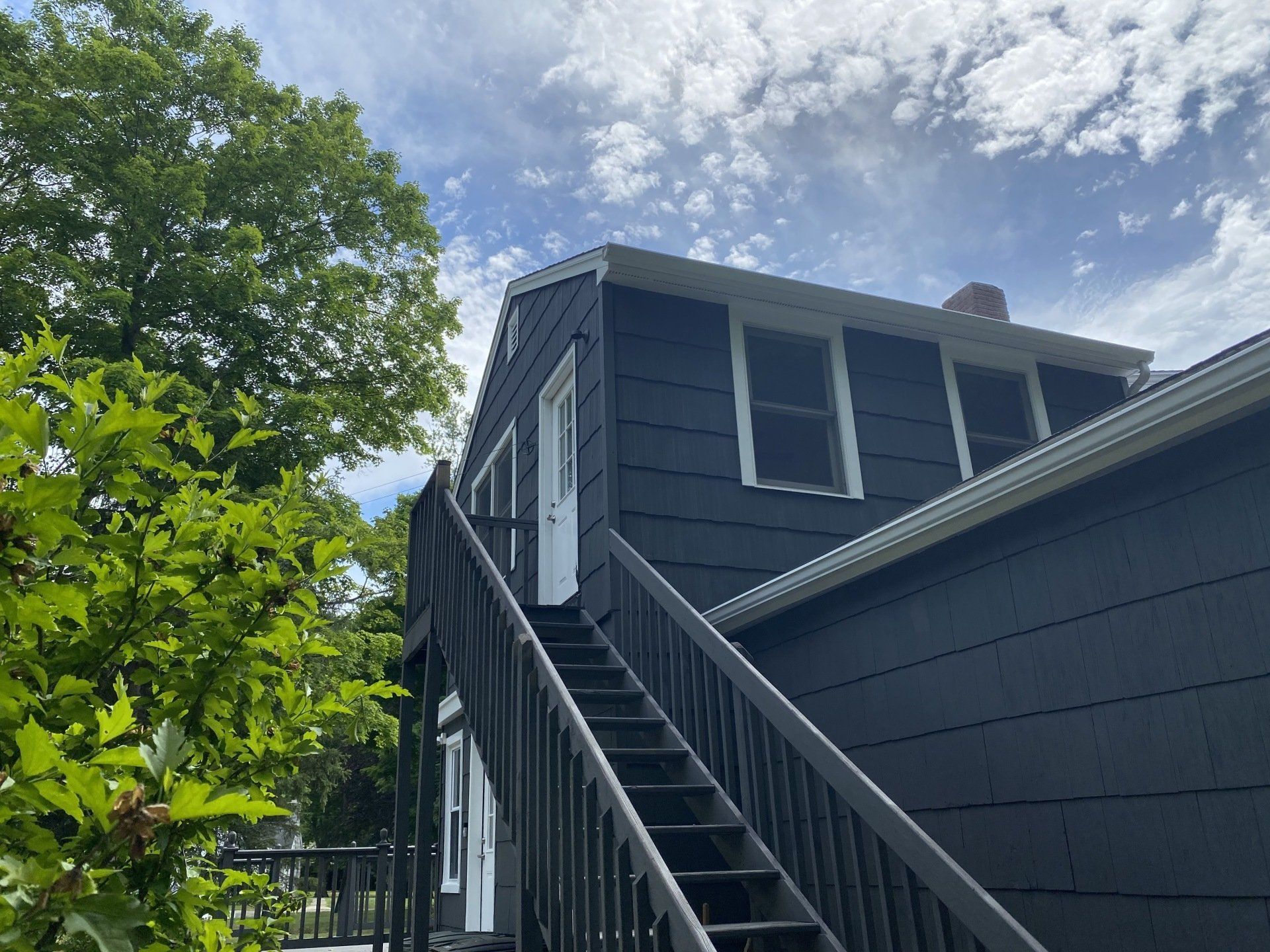 Black building exterior with outdoor stairs, white trim, and a partially cloudy sky.