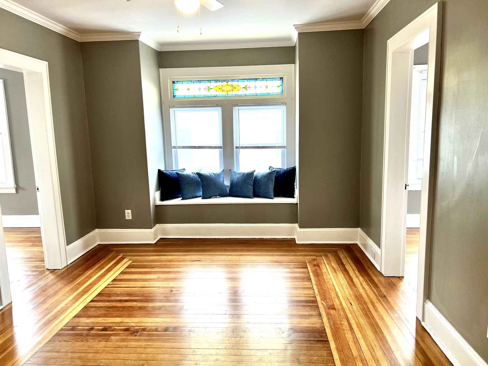Room with hardwood floors, a window seat with blue pillows, and stained glass.