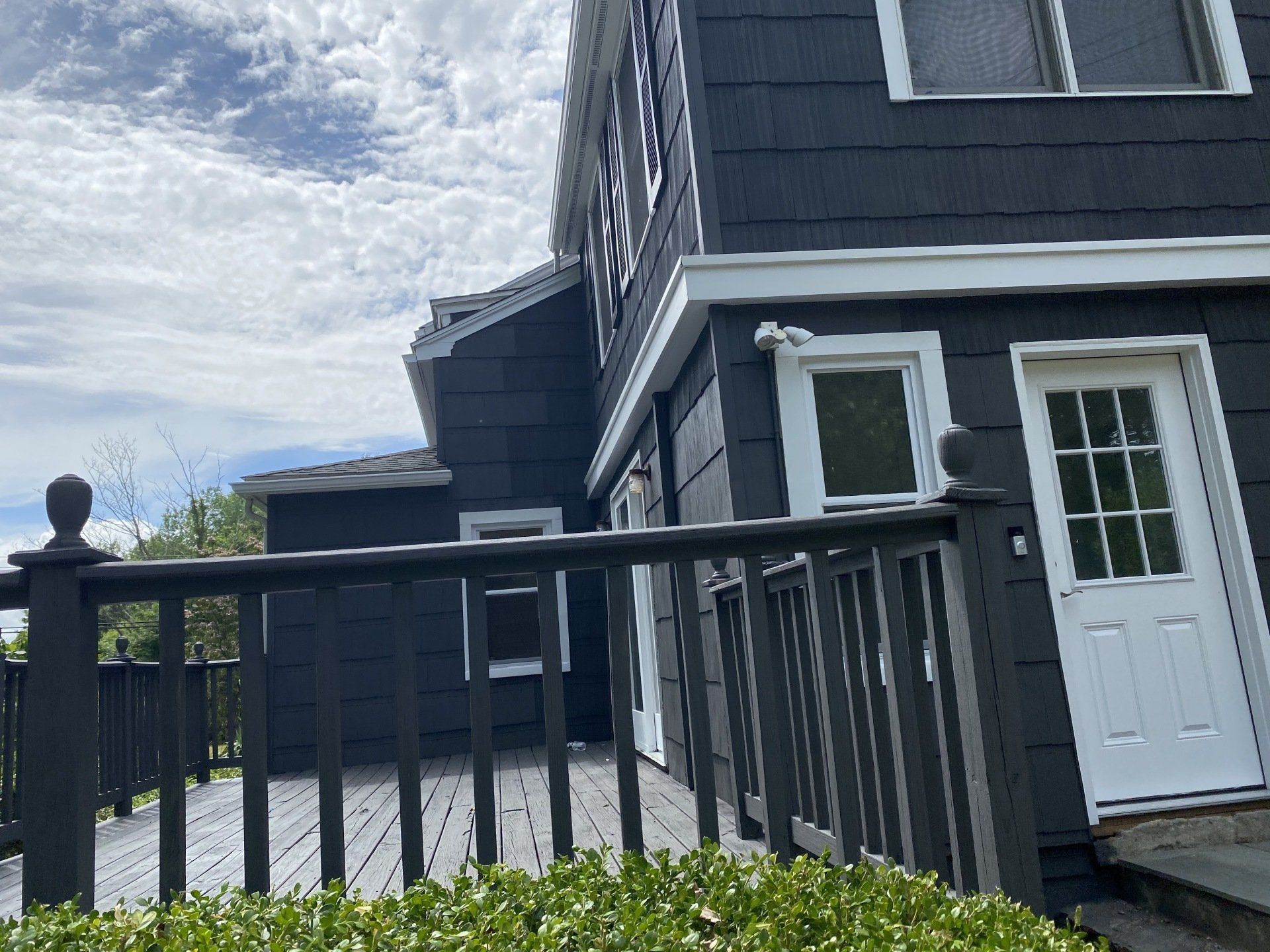 Dark gray house with a deck and white door under a cloudy sky.