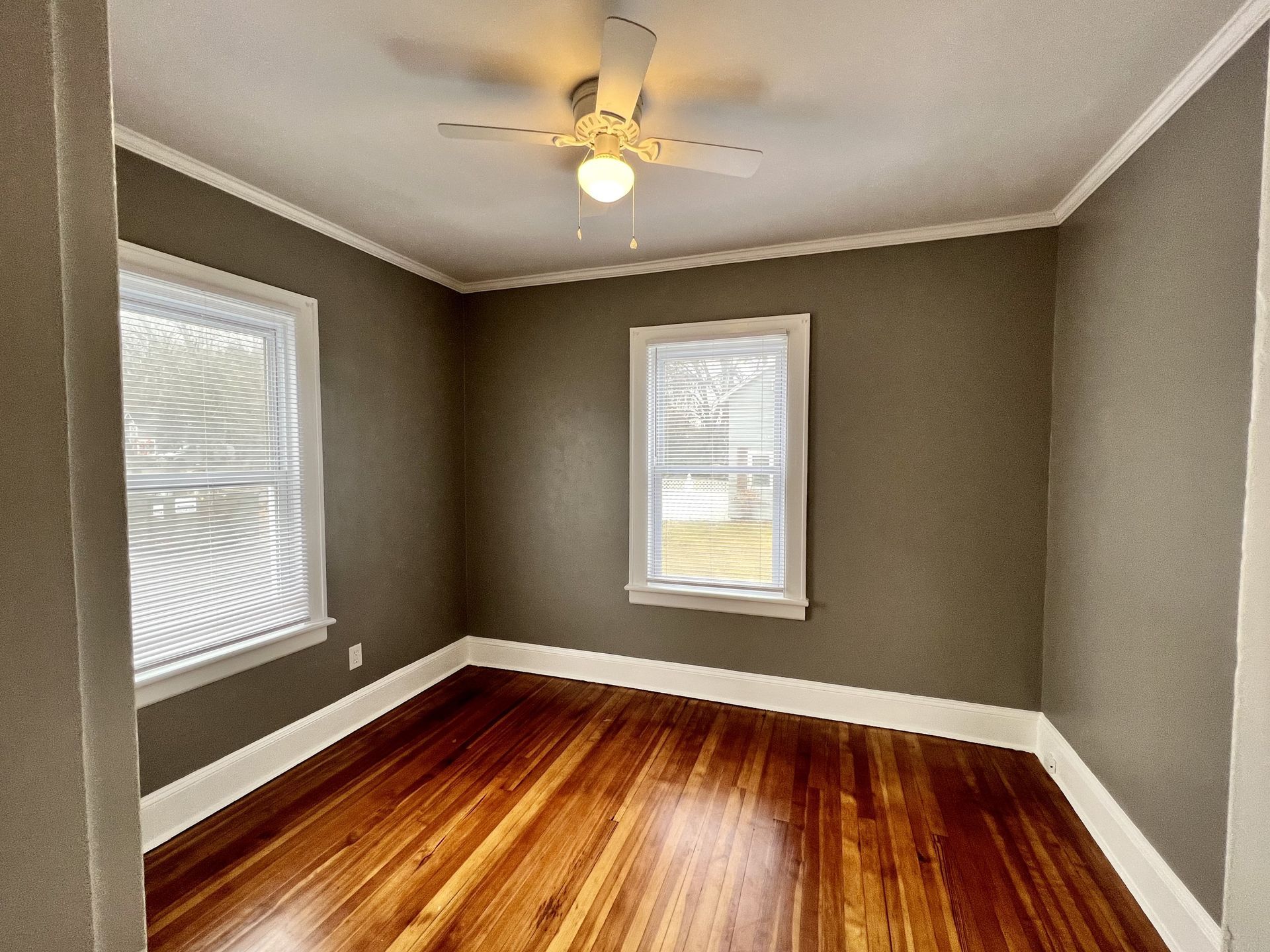 Empty bedroom with hardwood floors, two windows, and olive-green walls.