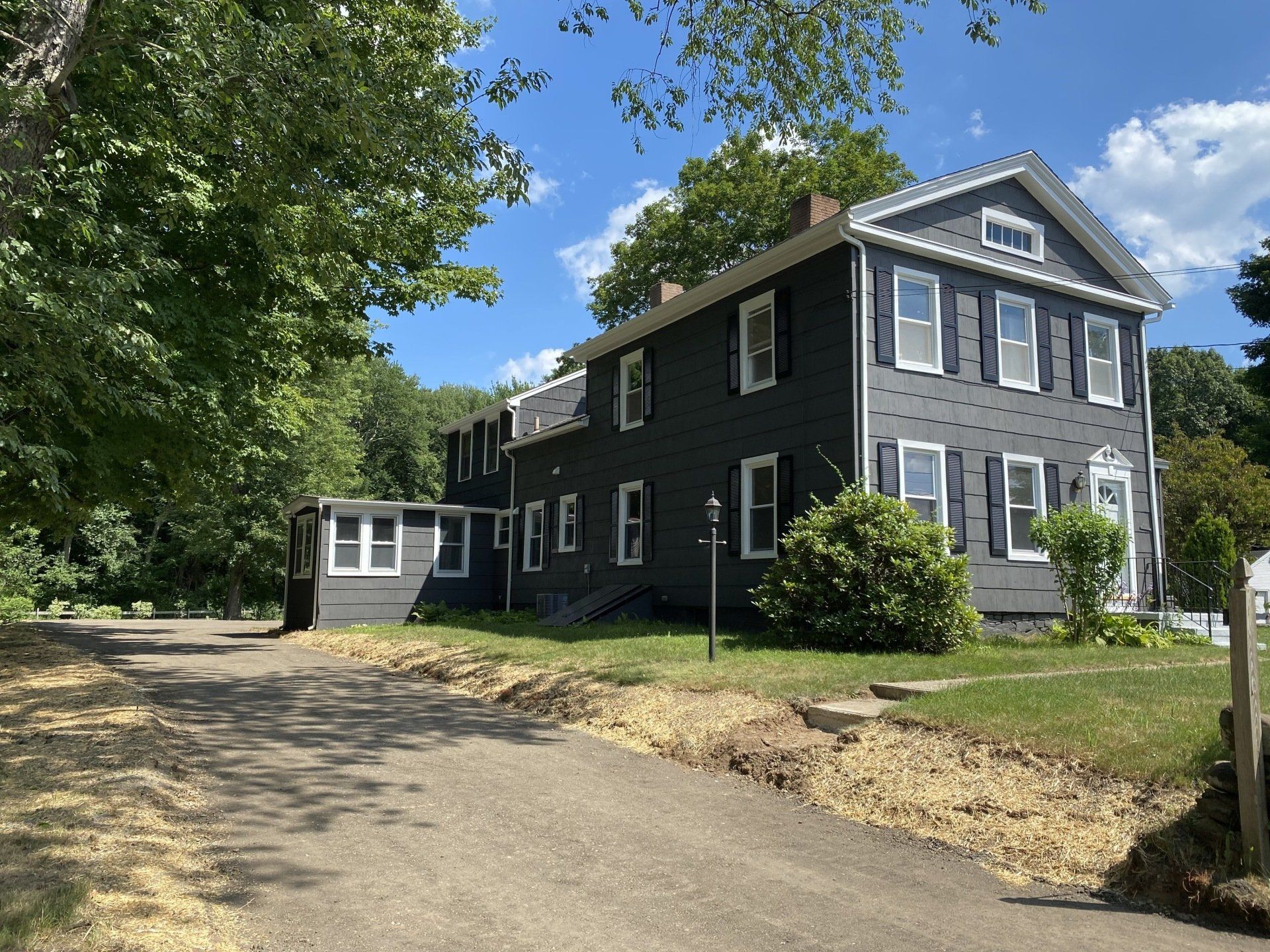 Dark gray house with white trim, black shutters, and a long driveway on a sunny day.