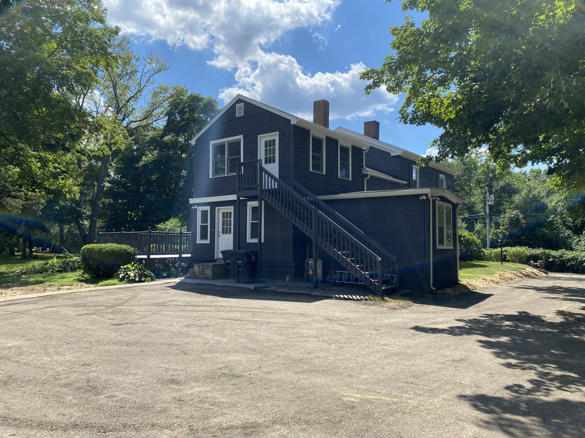 Two-story dark house with exterior stairs, white trim, and a small deck under a blue sky.