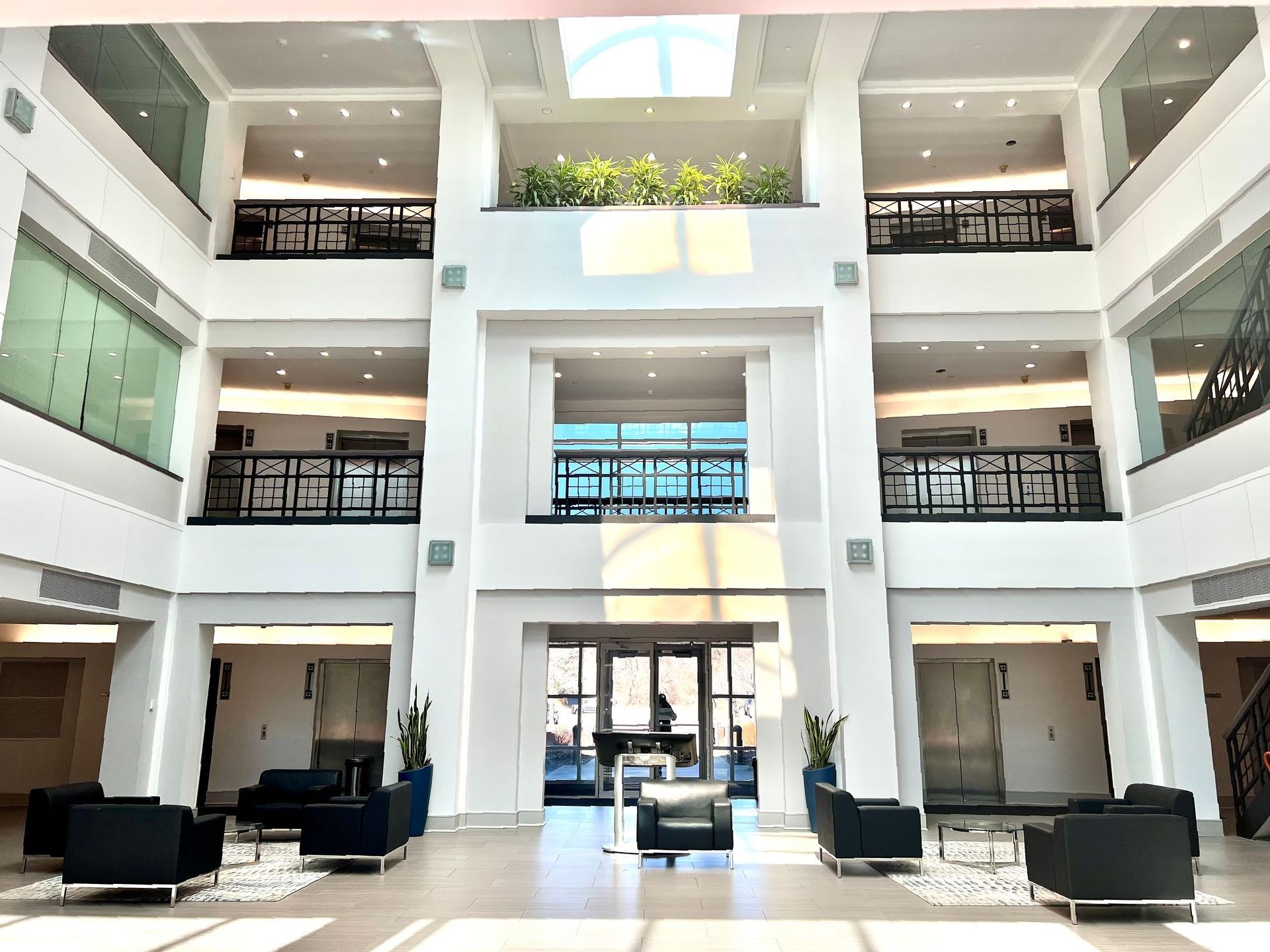 Interior lobby with multiple levels, white walls, black furniture, and natural light.