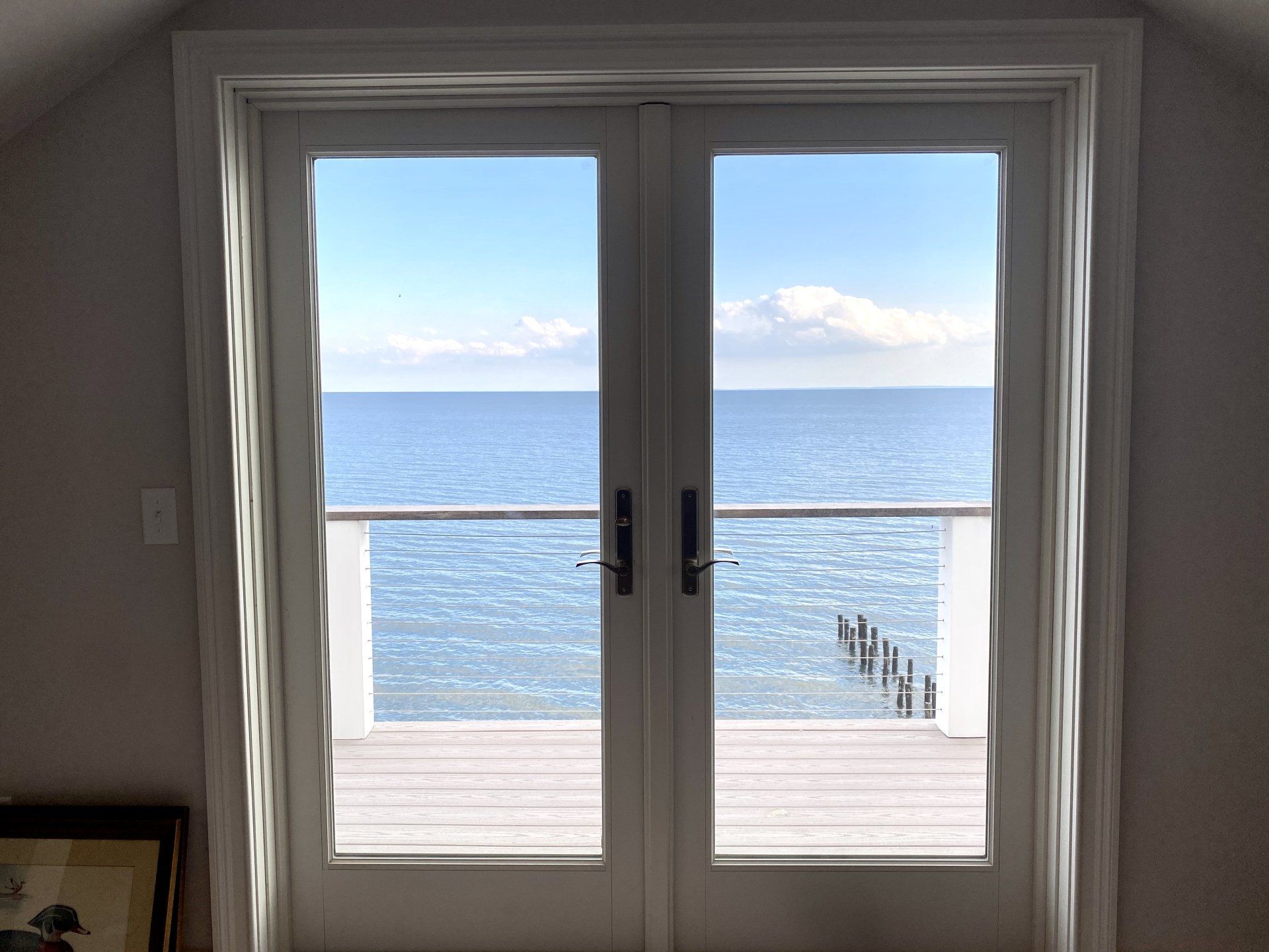 White double doors open to a serene ocean view. A deck and railing are visible.