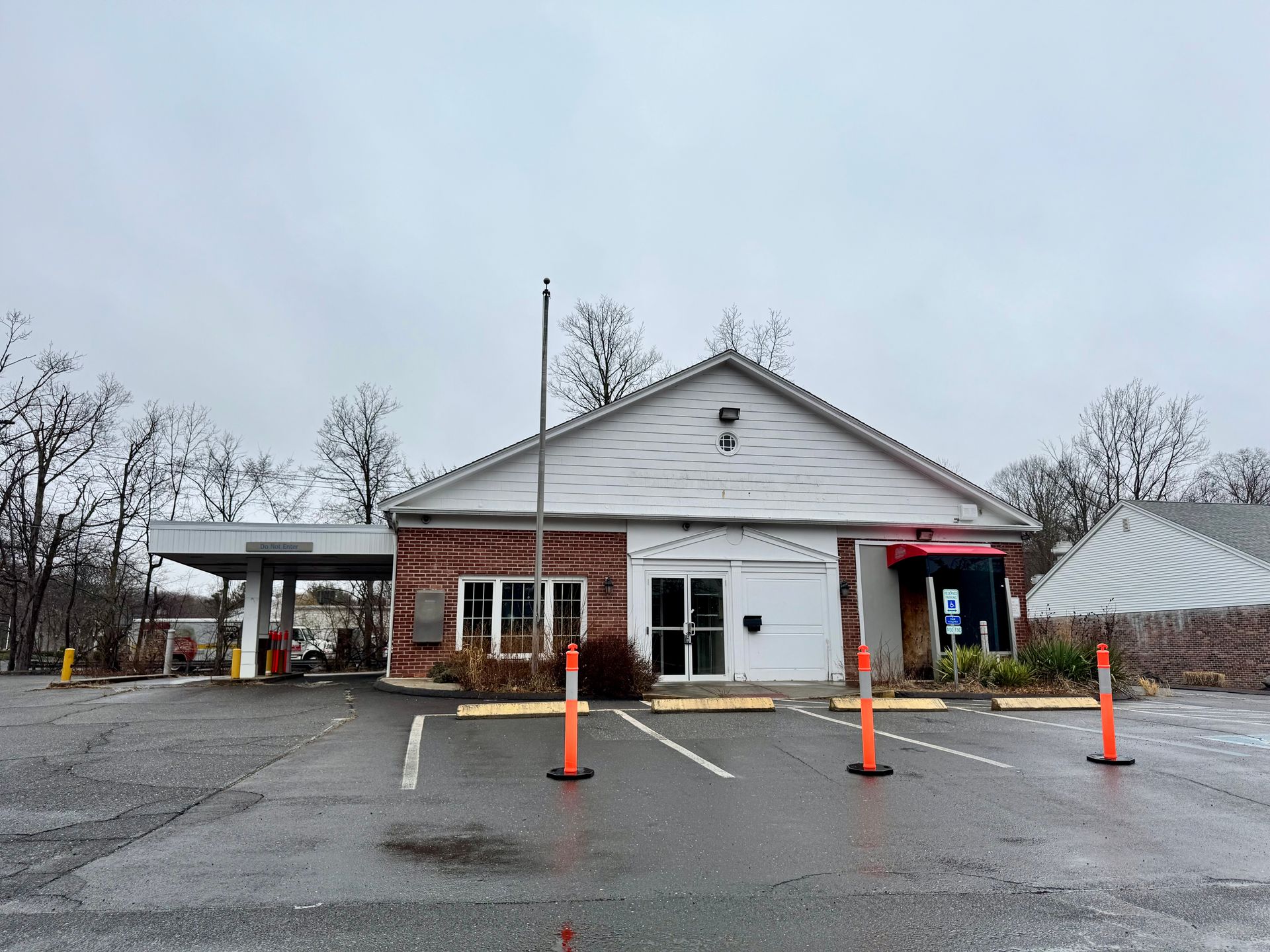 Bank exterior on a cloudy day, with a drive-up lane on the left and a striped umbrella on the right.