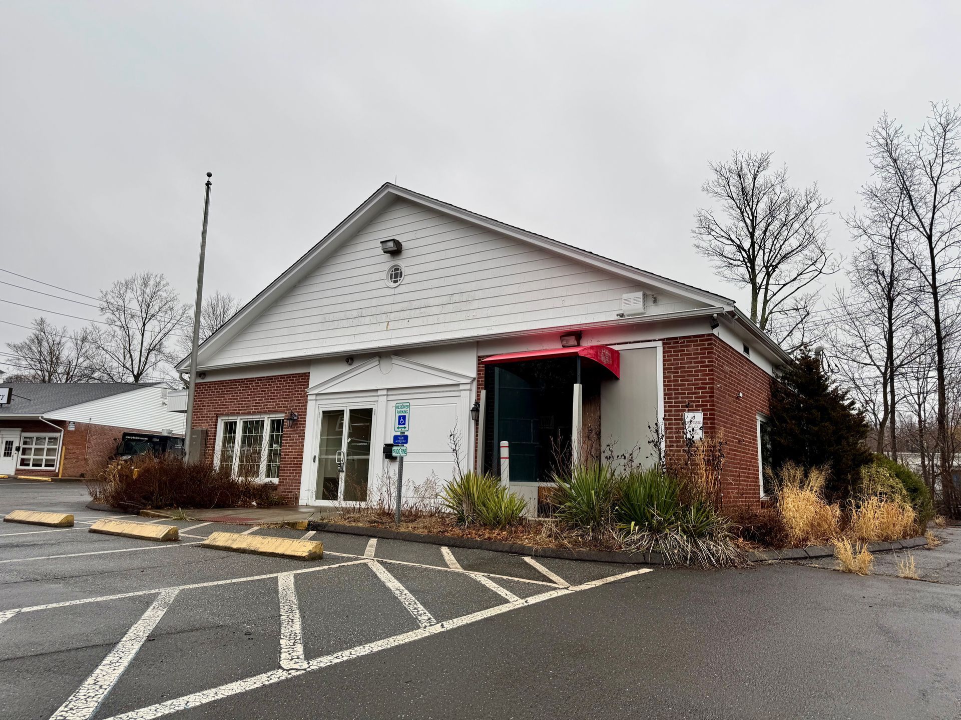 A one-story building with a red awning, red brick sides, and a wheelchair parking space on a cloudy day.