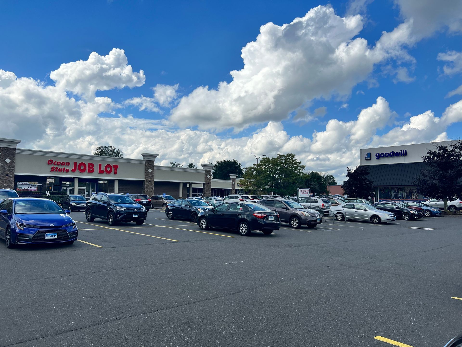Shopping center exterior with cars in the parking lot. Stores include Ocean State Job Lot and Goodwill on a sunny day.