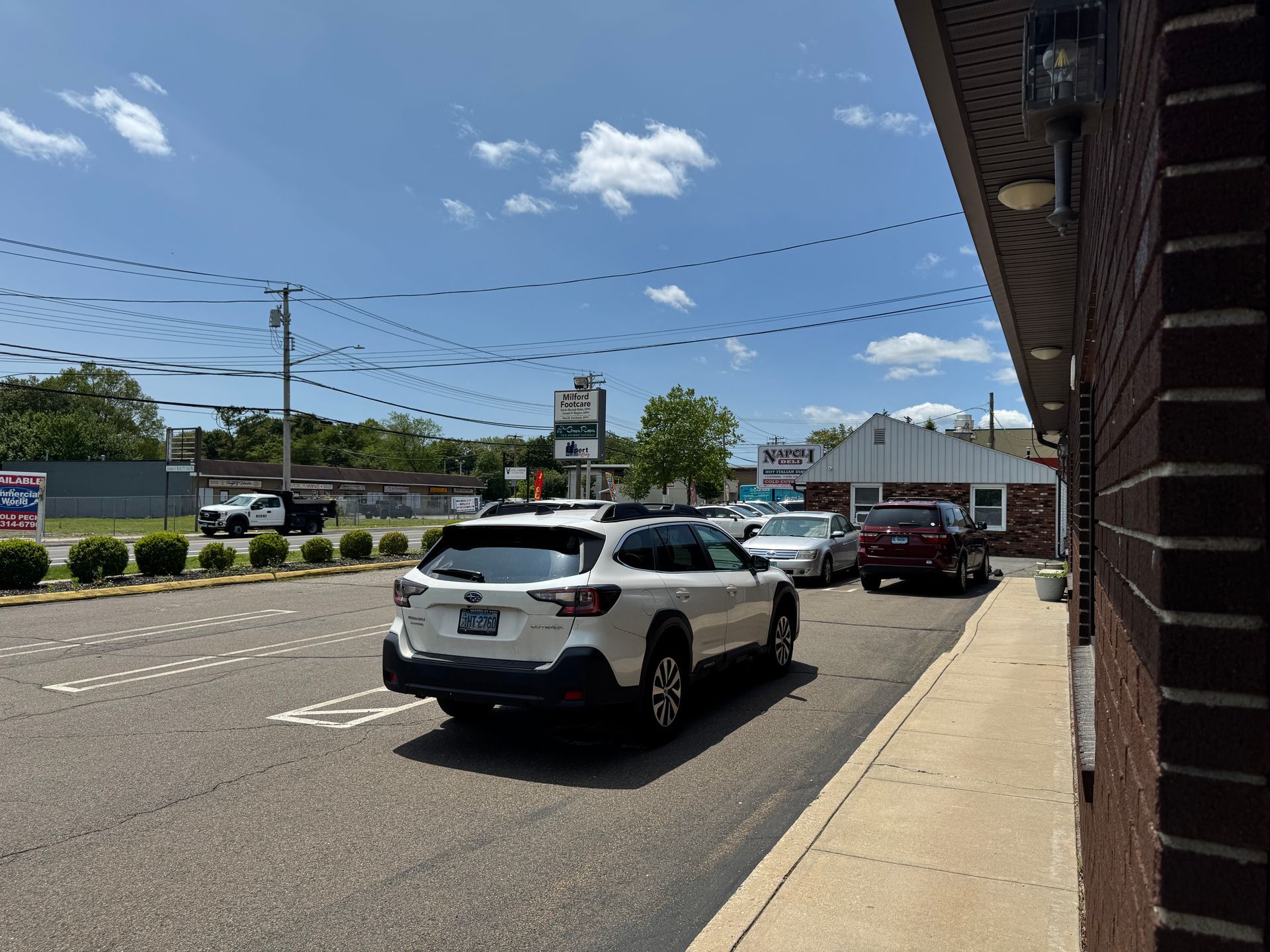 White SUV in a drive-thru, other cars in line. Sunny day, building with red brick.