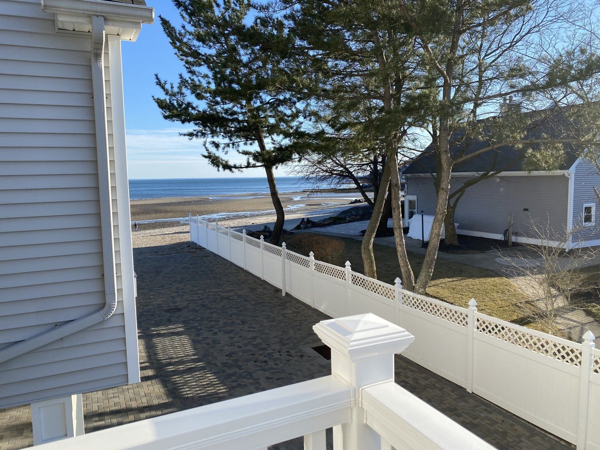 Beachfront view: white fence, sandy yard, ocean, house.