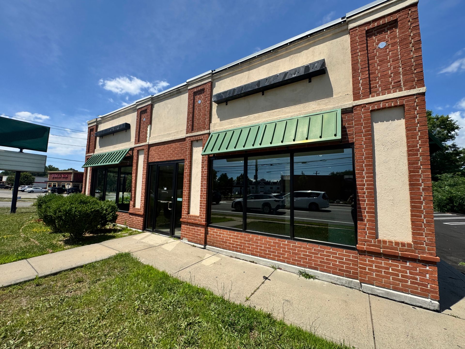 Storefront with brick accents, beige facade, green awnings, and large windows on a sunny day.