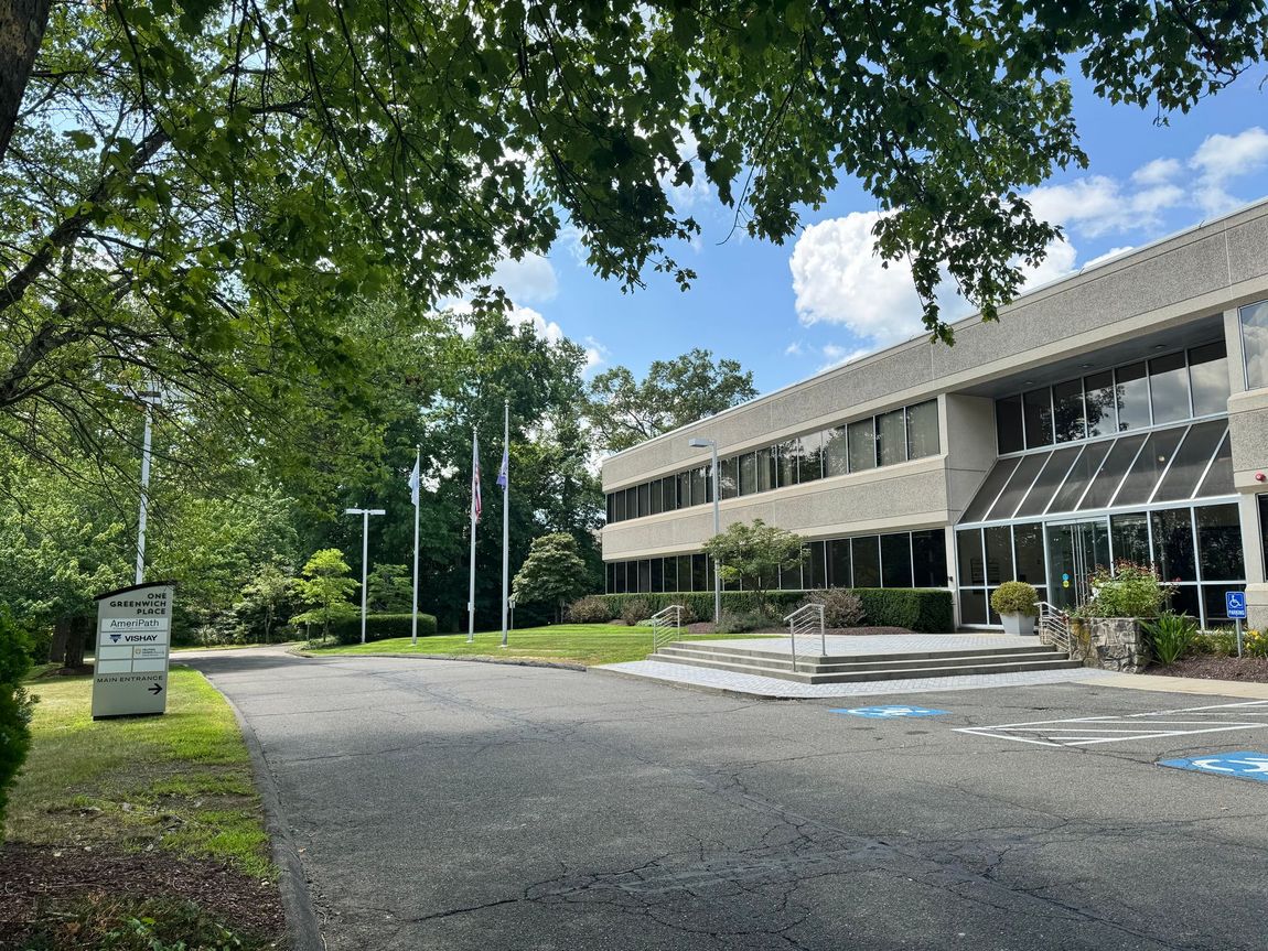 Office building exterior with trees, flags, and a paved driveway under a blue sky.