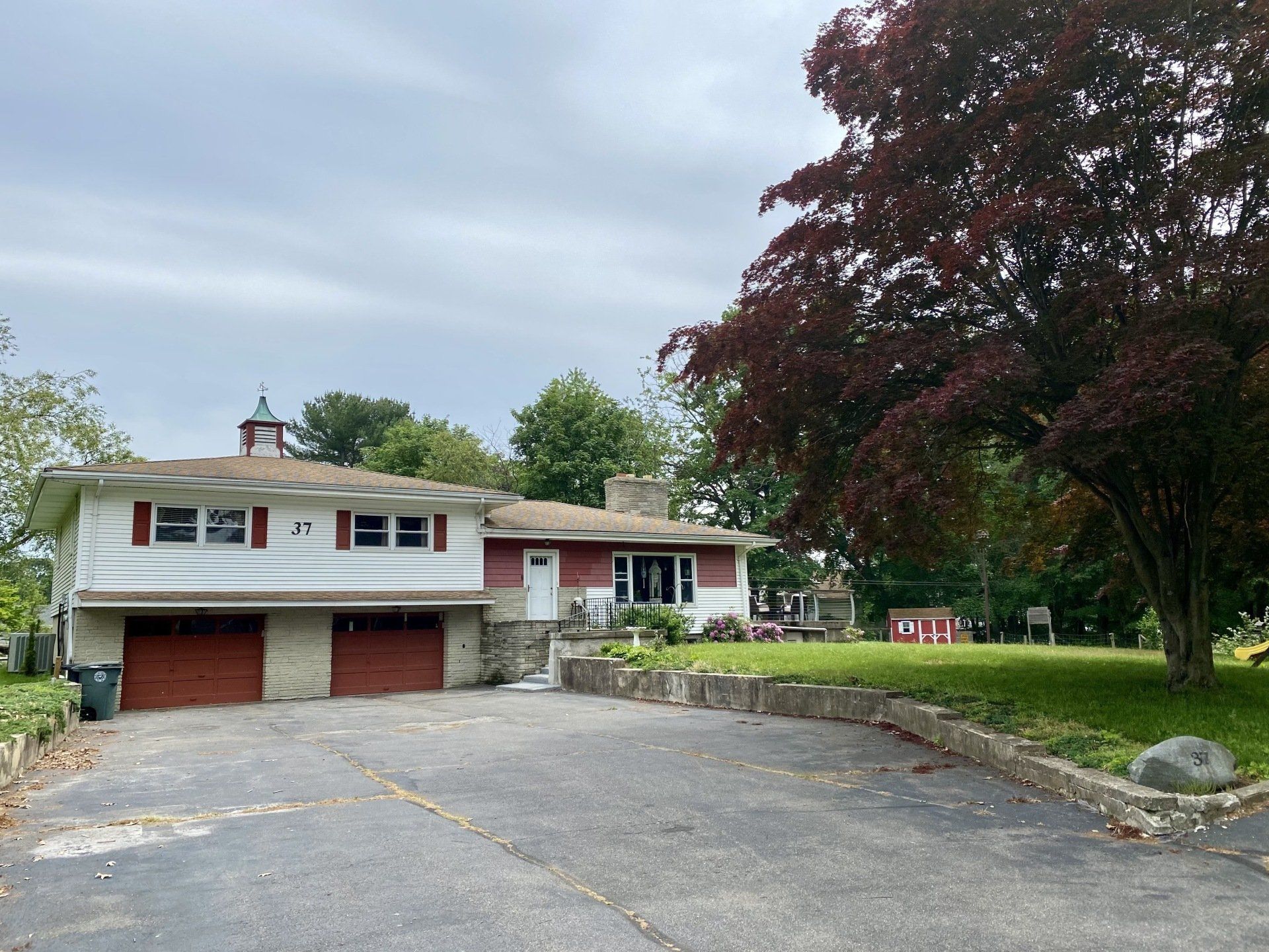 Two-story house with red garage doors and a red trim with a tree on the right side and a driveway.