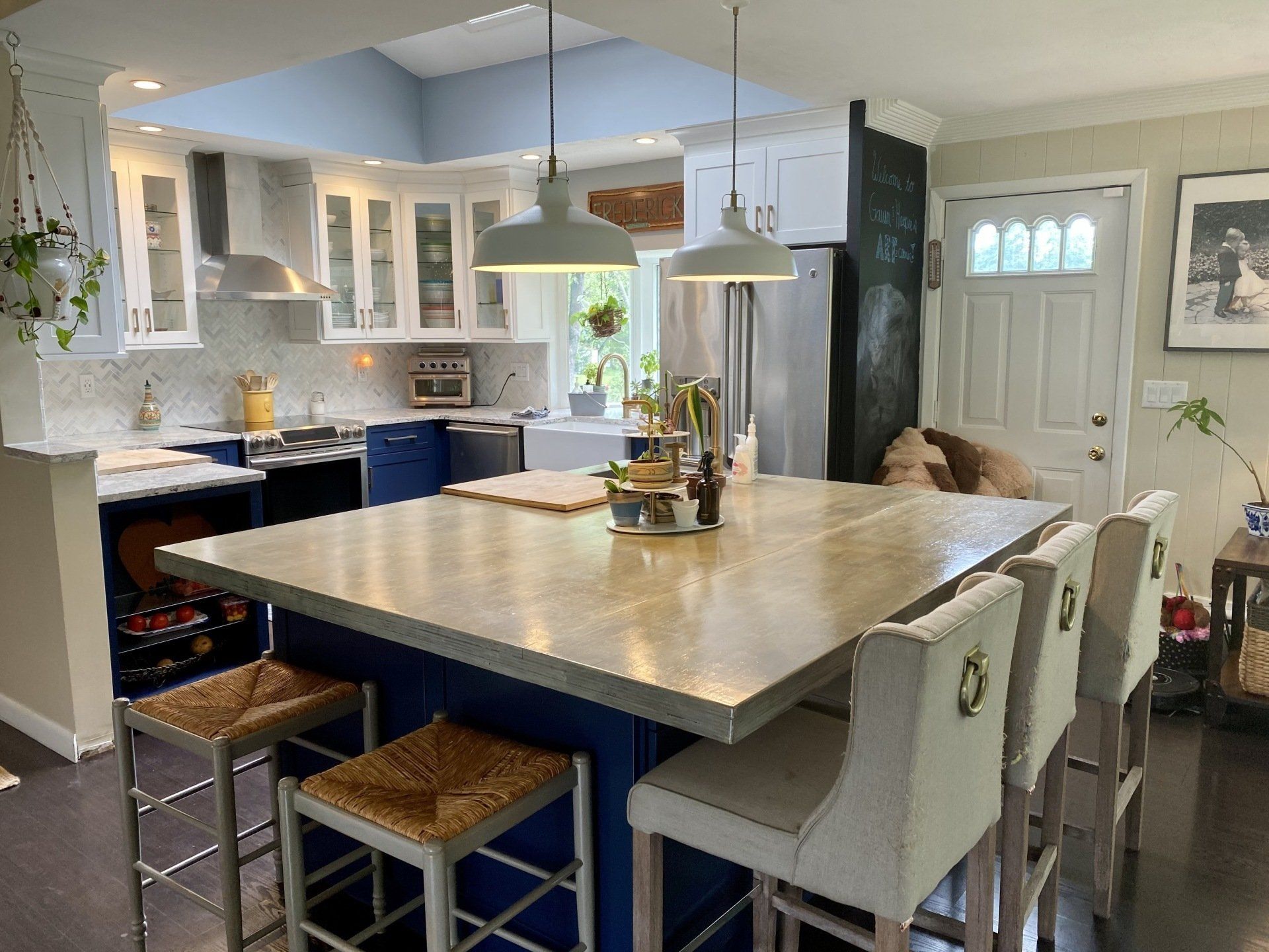 Bright kitchen with blue island and white cabinets; island has stools, a sink, and a stainless steel refrigerator.