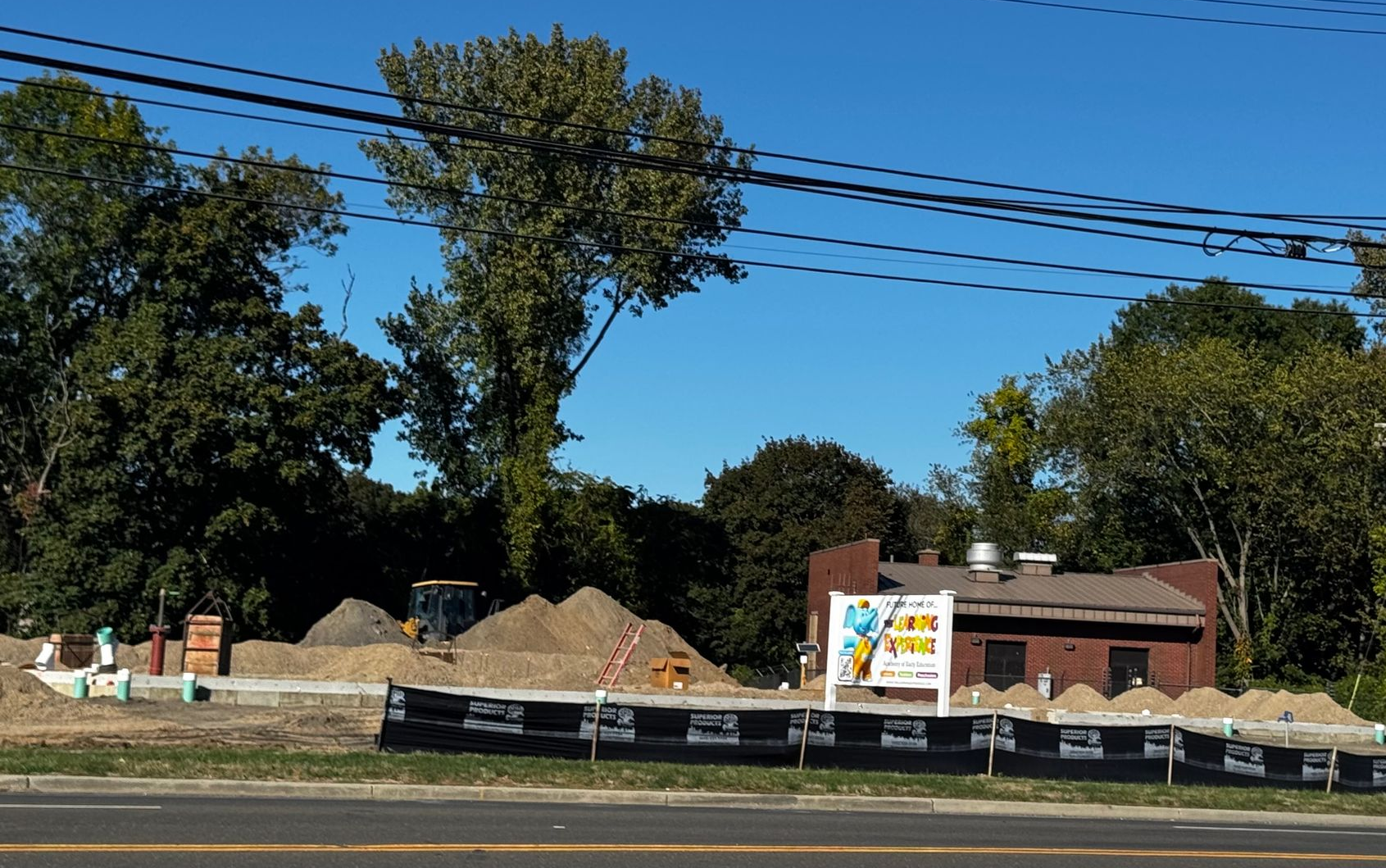 Construction site with piles of dirt and a small brick building; clear blue sky.
