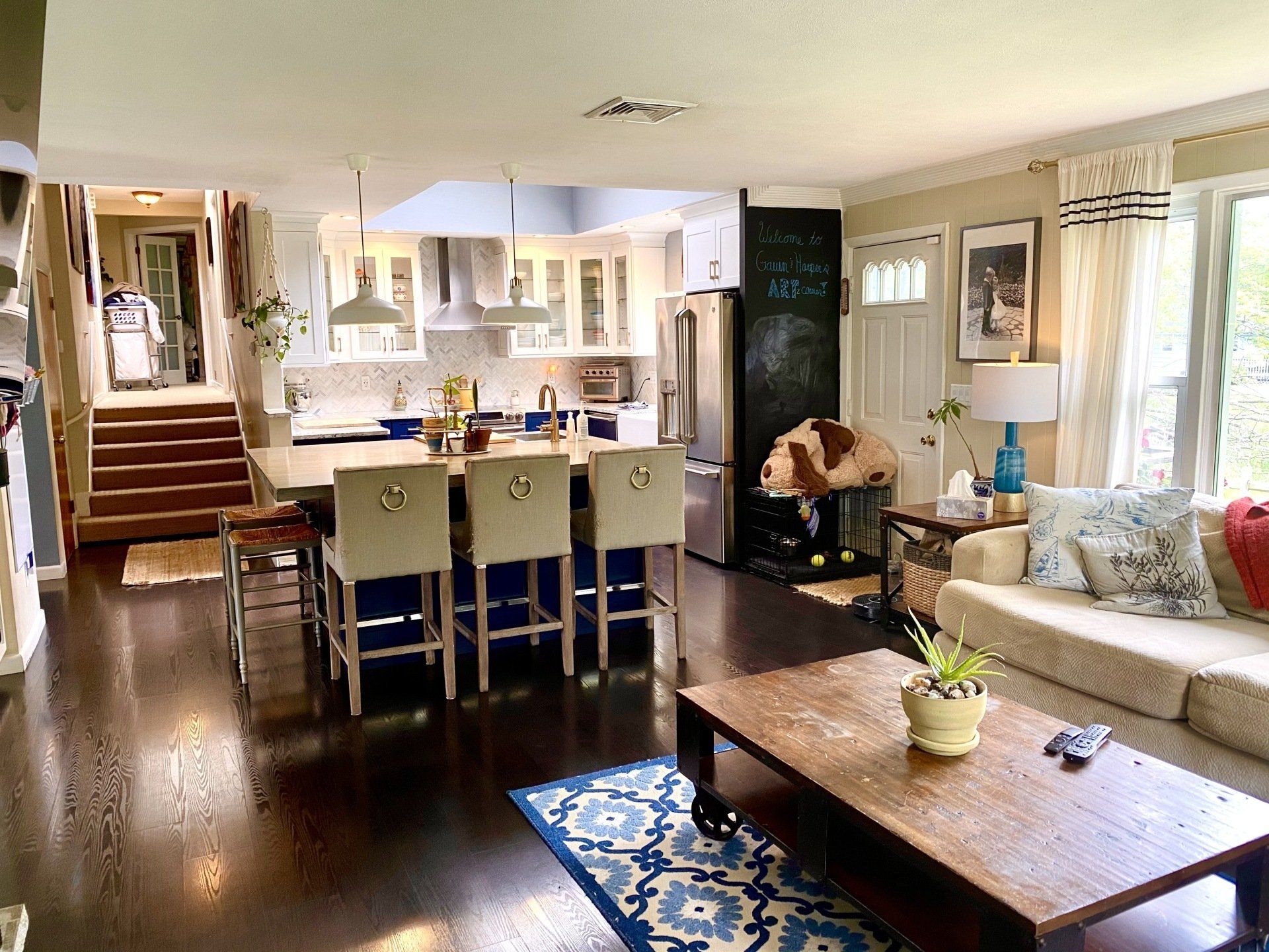 Open-concept kitchen and living room with dark wood floors, white cabinets, and a dog resting in a crate.