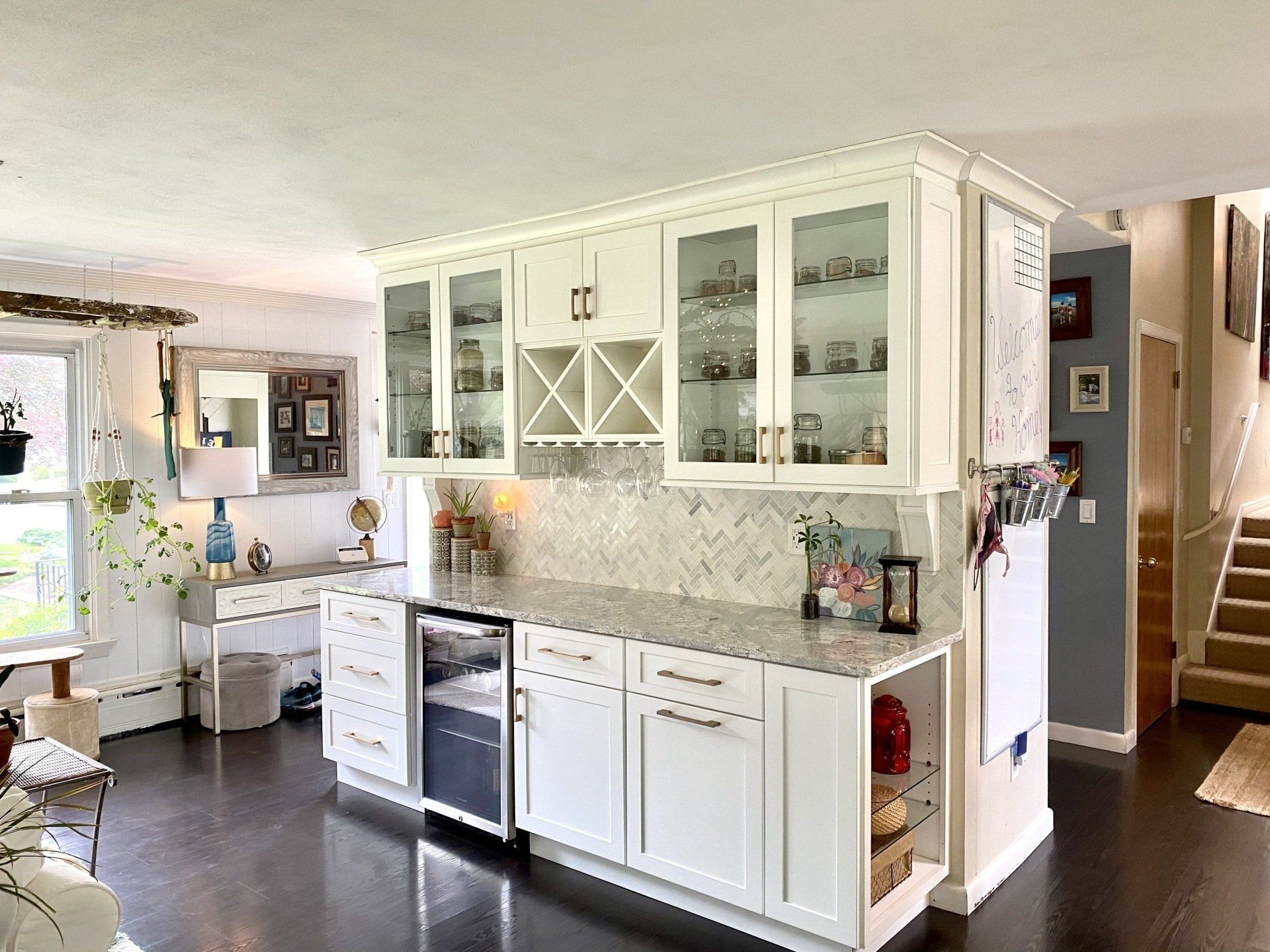 White kitchen island with cabinets, wine rack, and beverage fridge. Dark wood floors, bright room.