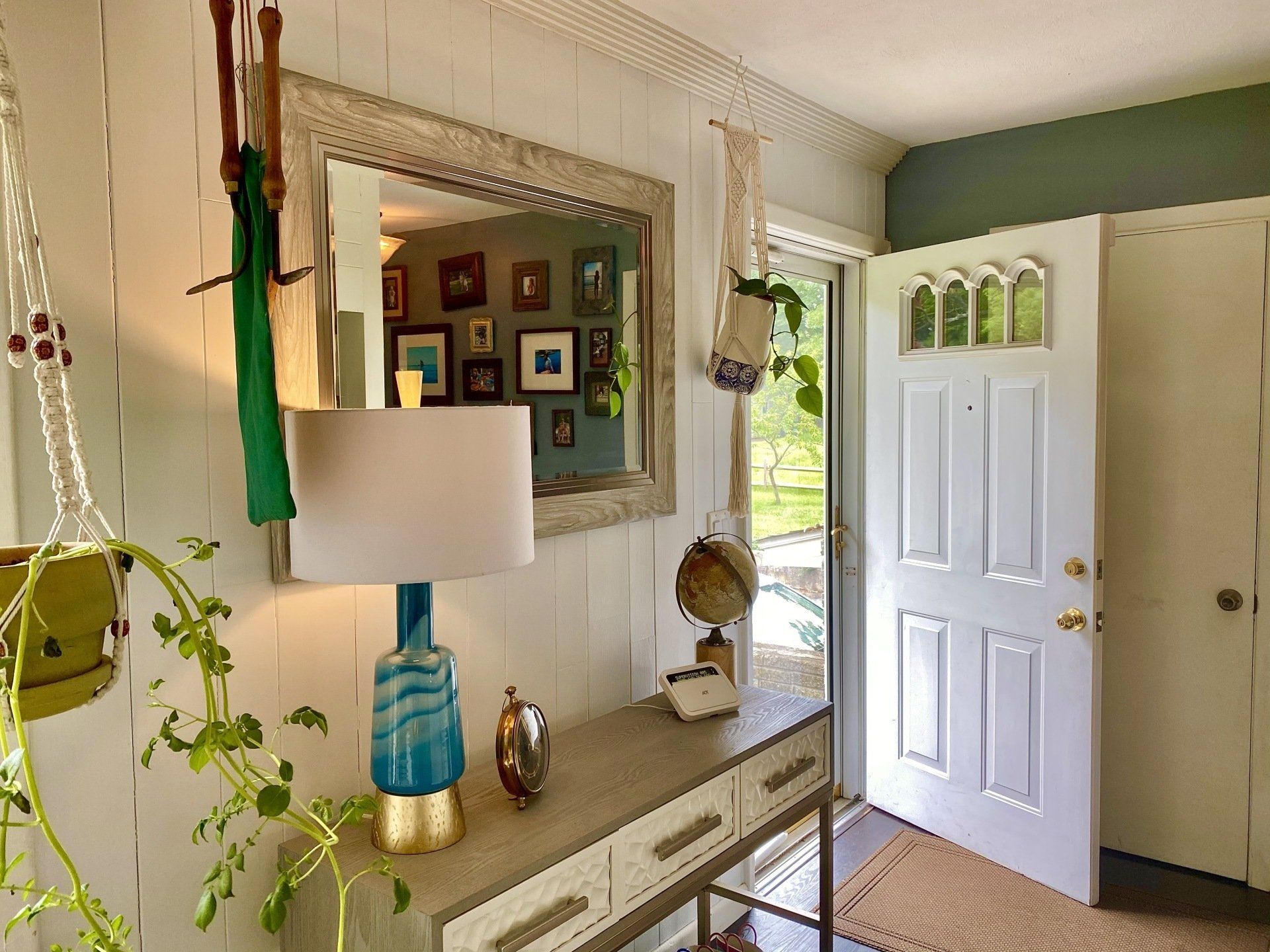 Cozy entryway with a console table, mirror, and open door. Plants and vintage decor in a bright room.