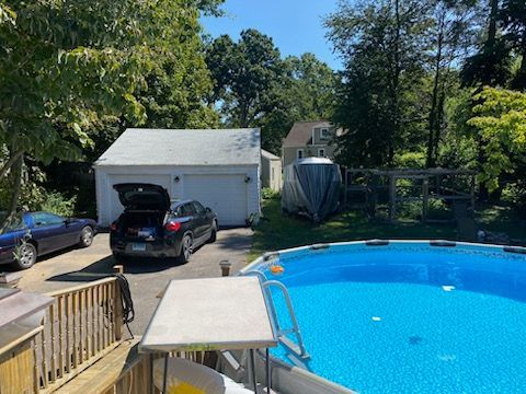 Backyard scene with pool, cars, garage, boat, and trees on a sunny day.
