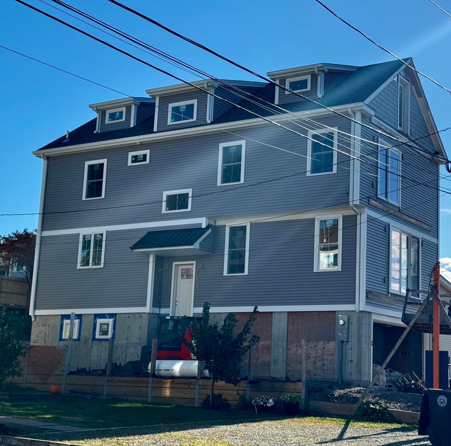 Three-story gray house under construction with multiple windows and a blue sky in the background.