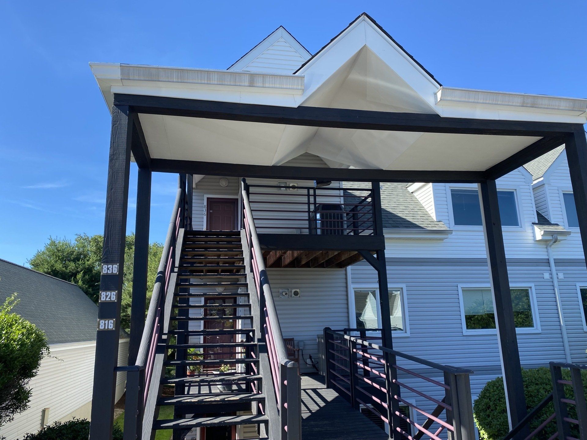Two-story building with black metal staircase and railing leading to a covered entrance. Blue sky background.