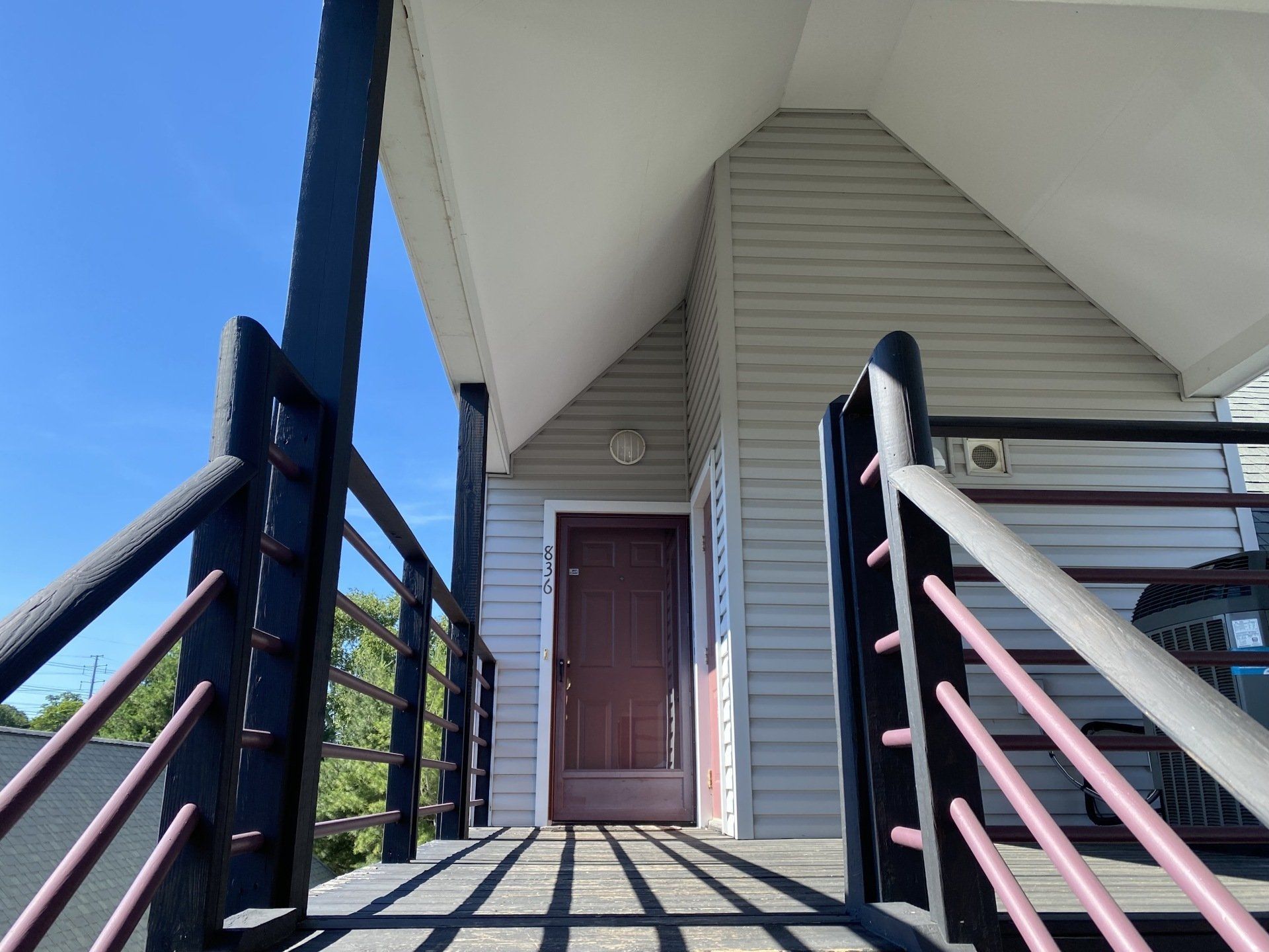 Exterior view of a porch with a brown door, black railing, gray siding, and a blue sky.