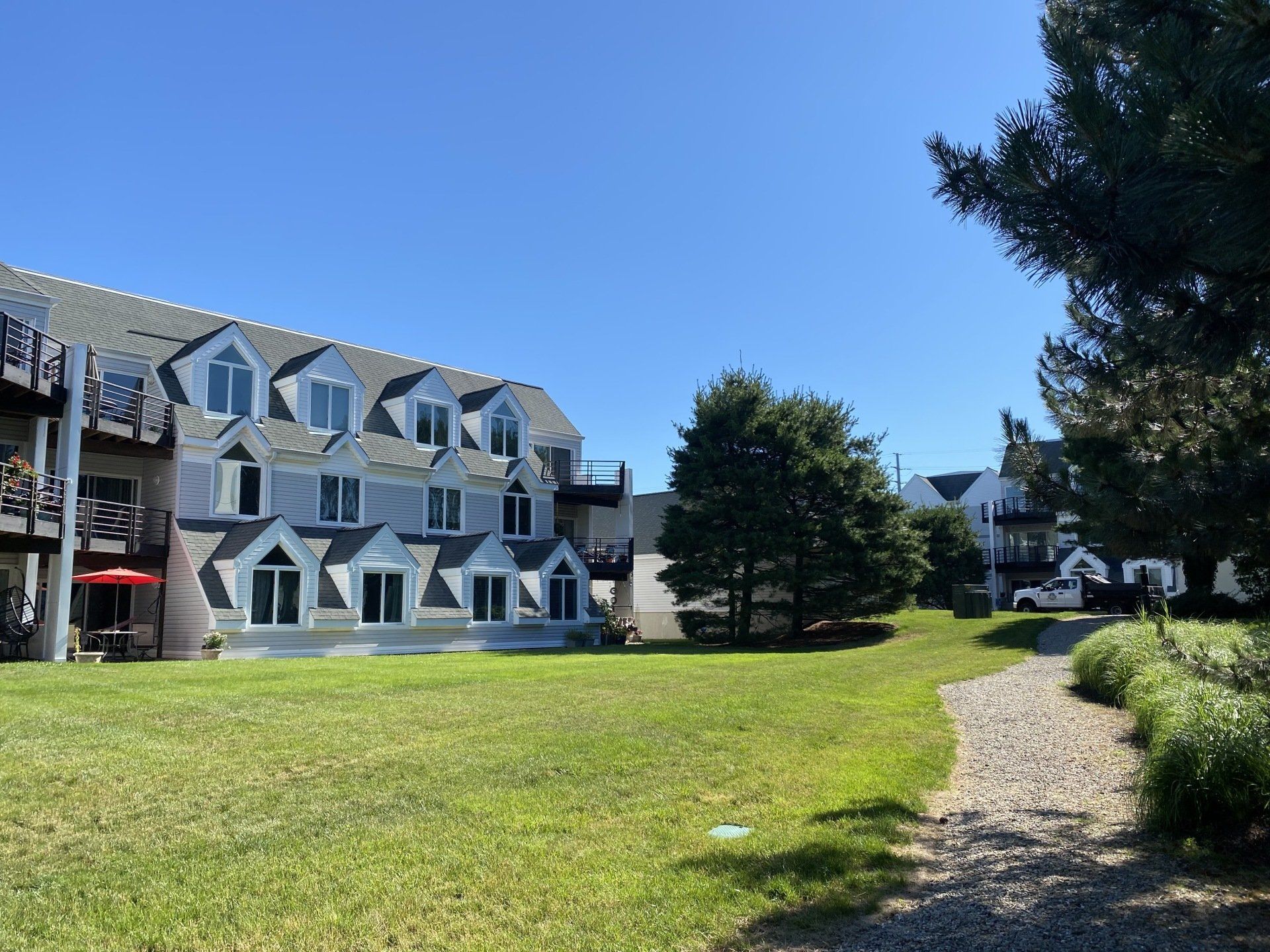 Apartment building with dormer windows, blue sky, and green lawn.